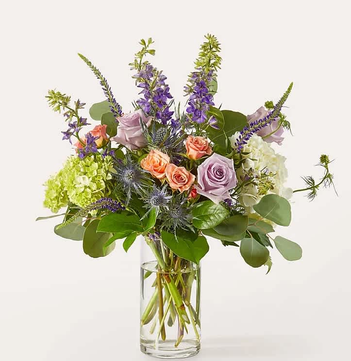 Mixed bouquet of roses, hydrangeas, and purple spikes in a clear glass vase