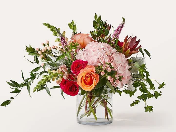 Mixed bouquet of pink, peach, and red flowers in a clear glass vase