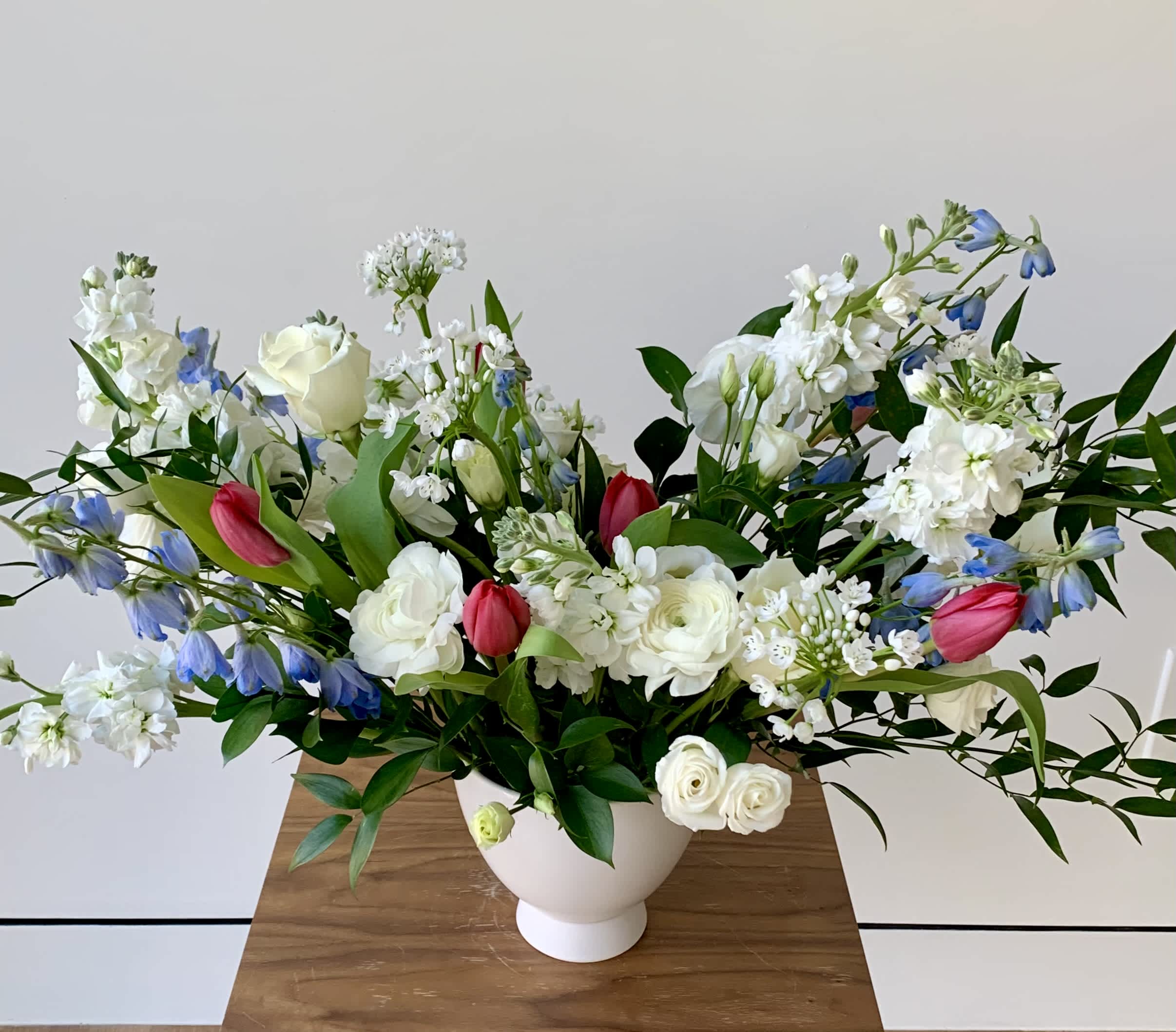 White and blue floral arrangement with pink tulips in a white vase