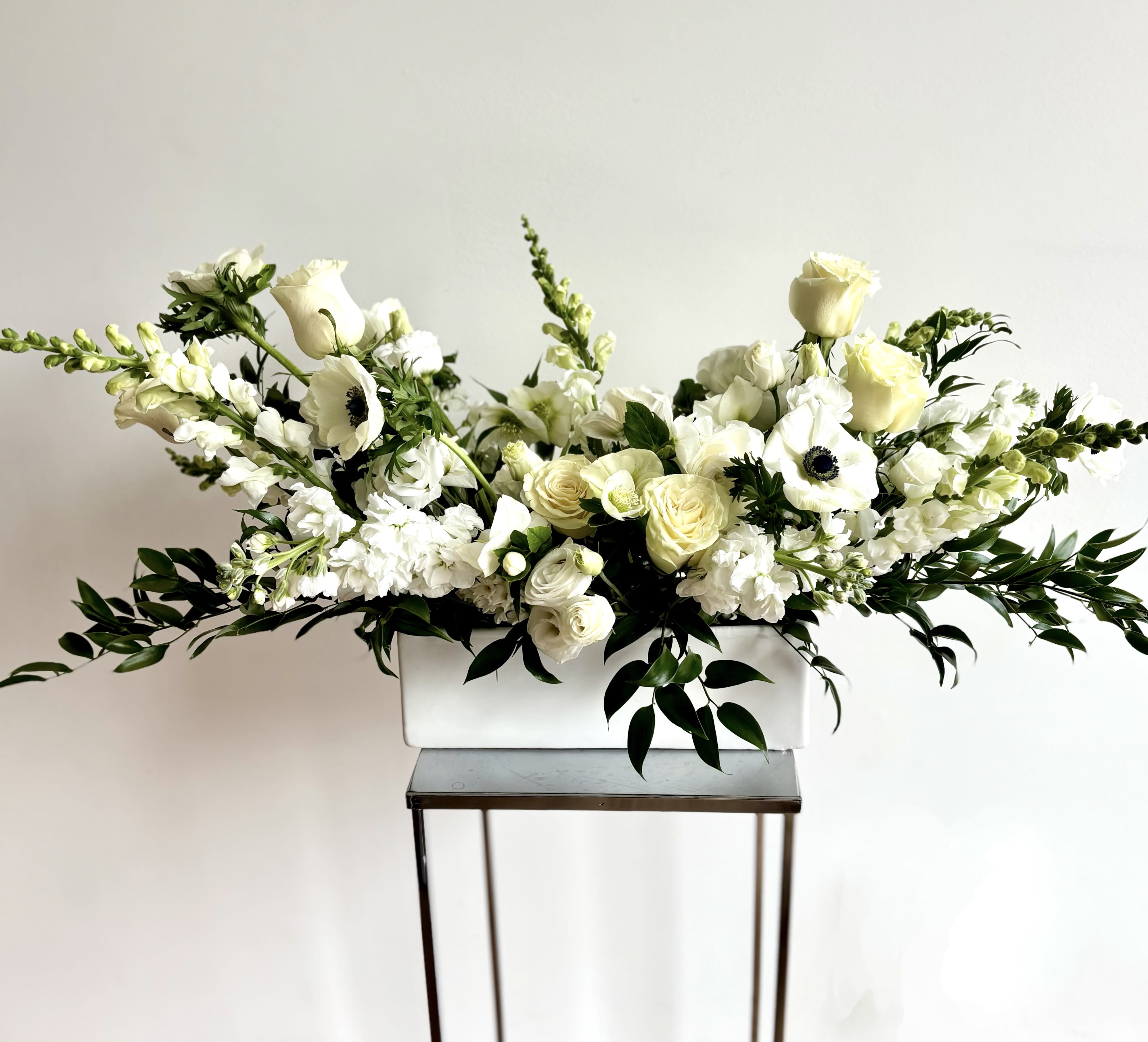 White floral arrangement in a rectangular vase with long greenery