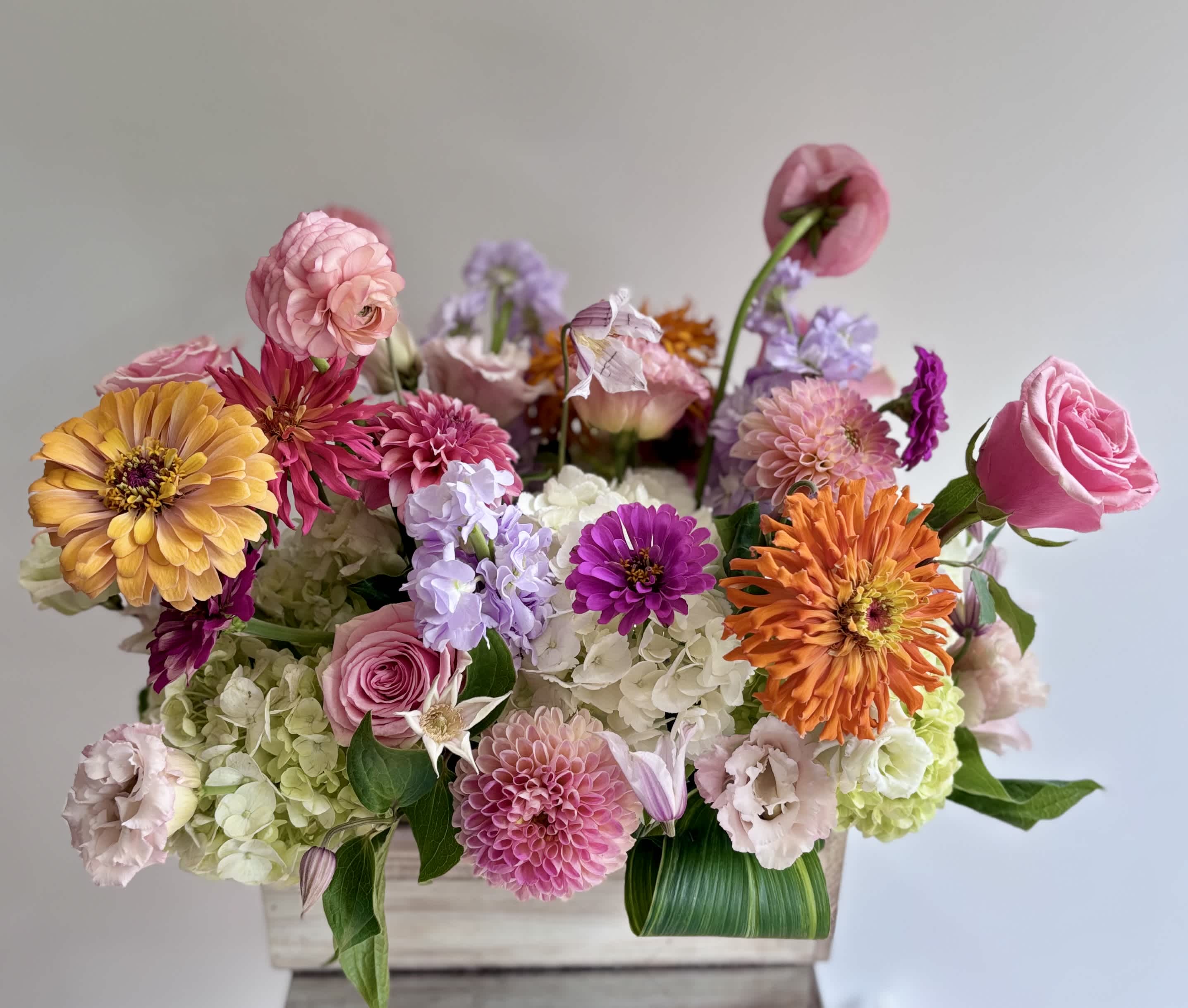 Mixed bouquet of pink, orange, and lavender flowers in a wooden box