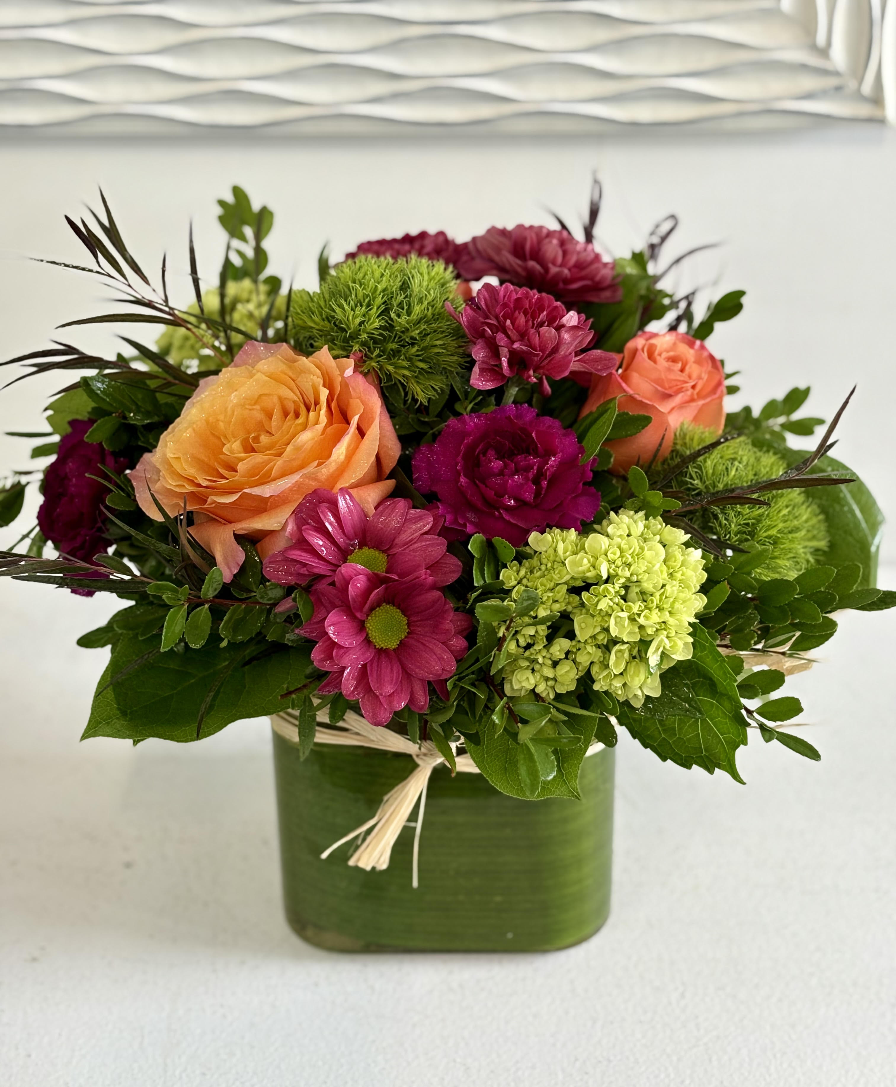 Mixed bouquet of orange and pink flowers in a green square vase