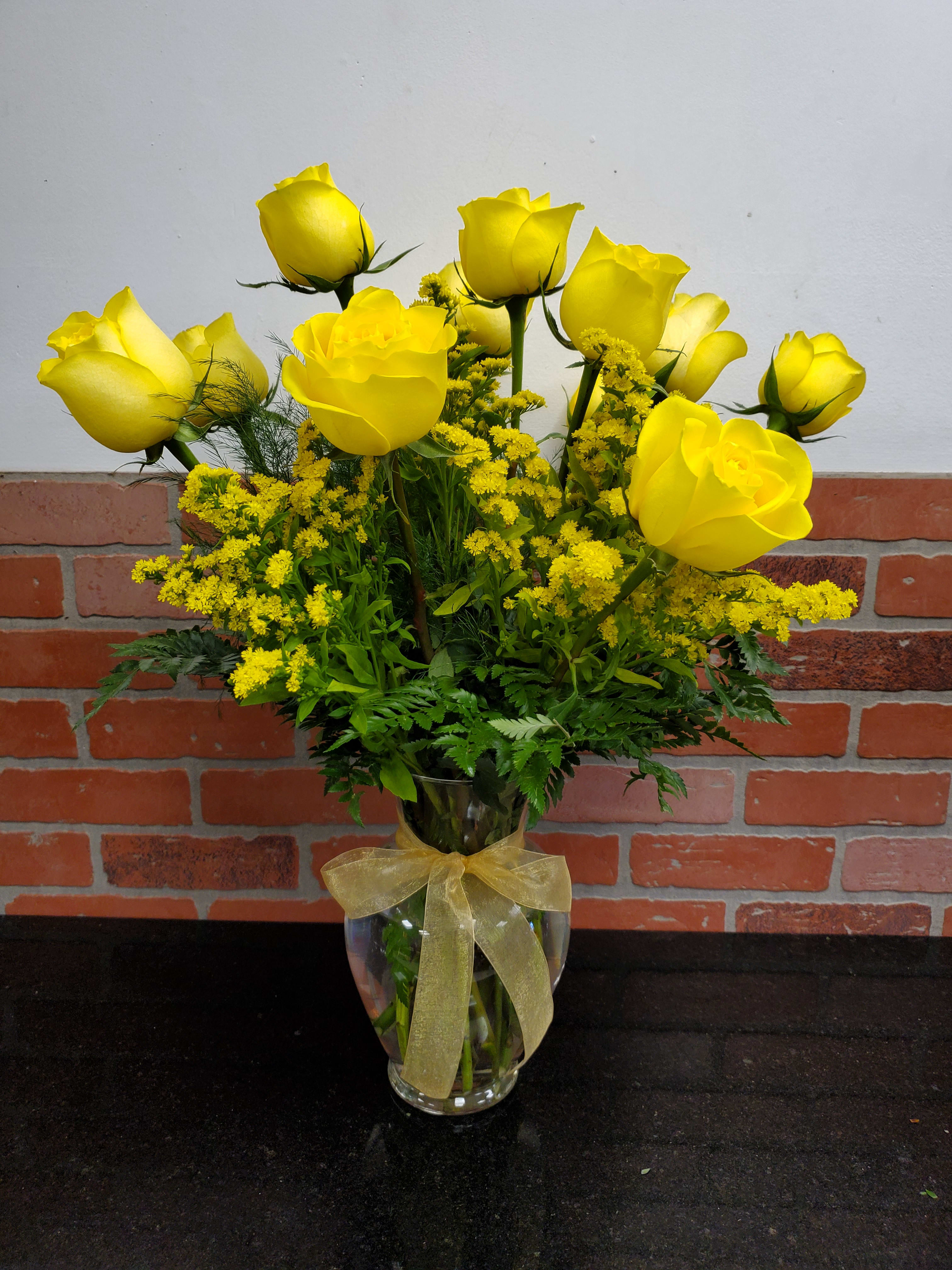 Arrangement of yellow roses with yellow filler flowers in a clear glass vase tied with a sheer gold bow.
