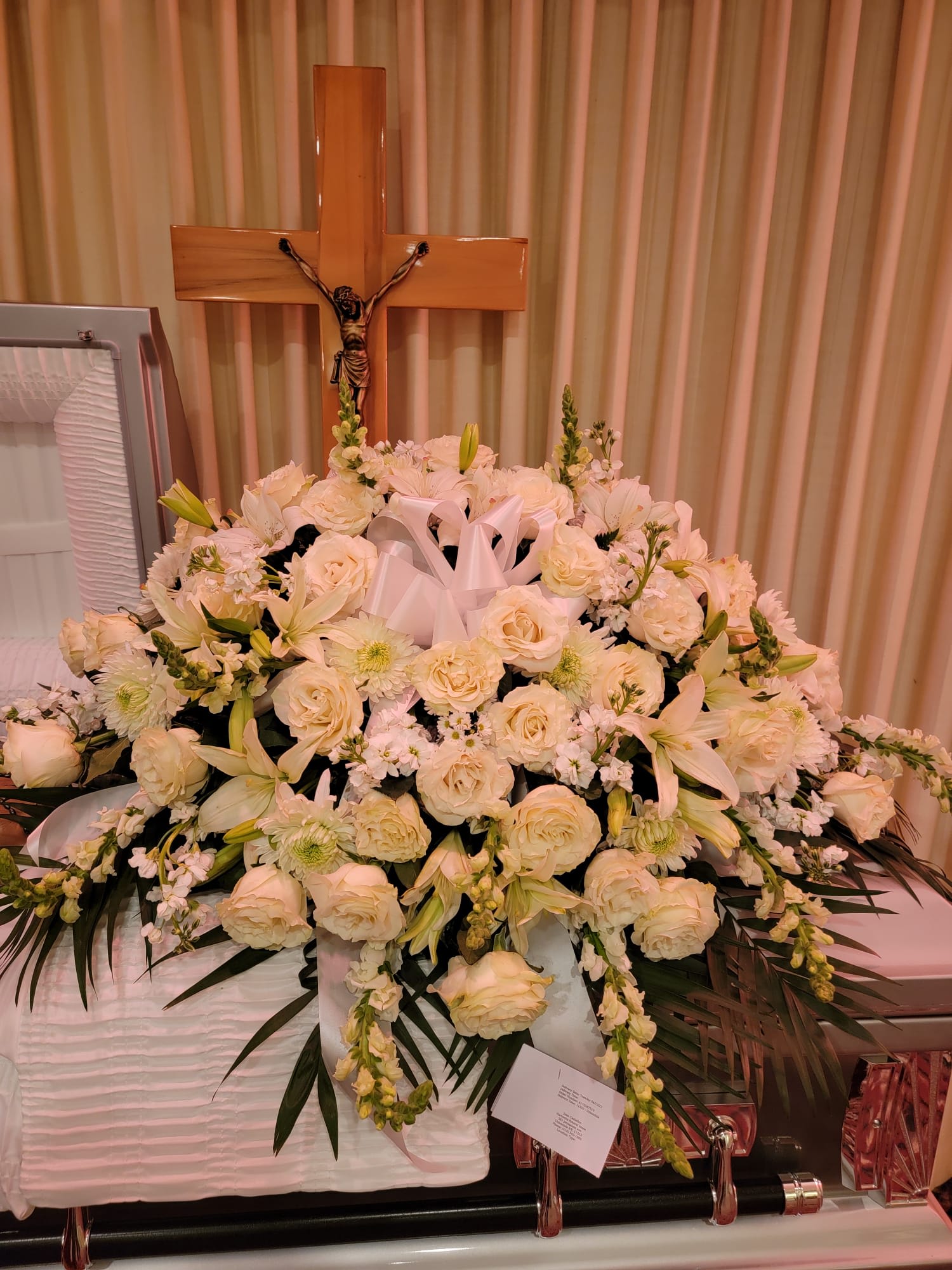 Large white and cream casket spray of roses and lilies in front of a wooden crucifix