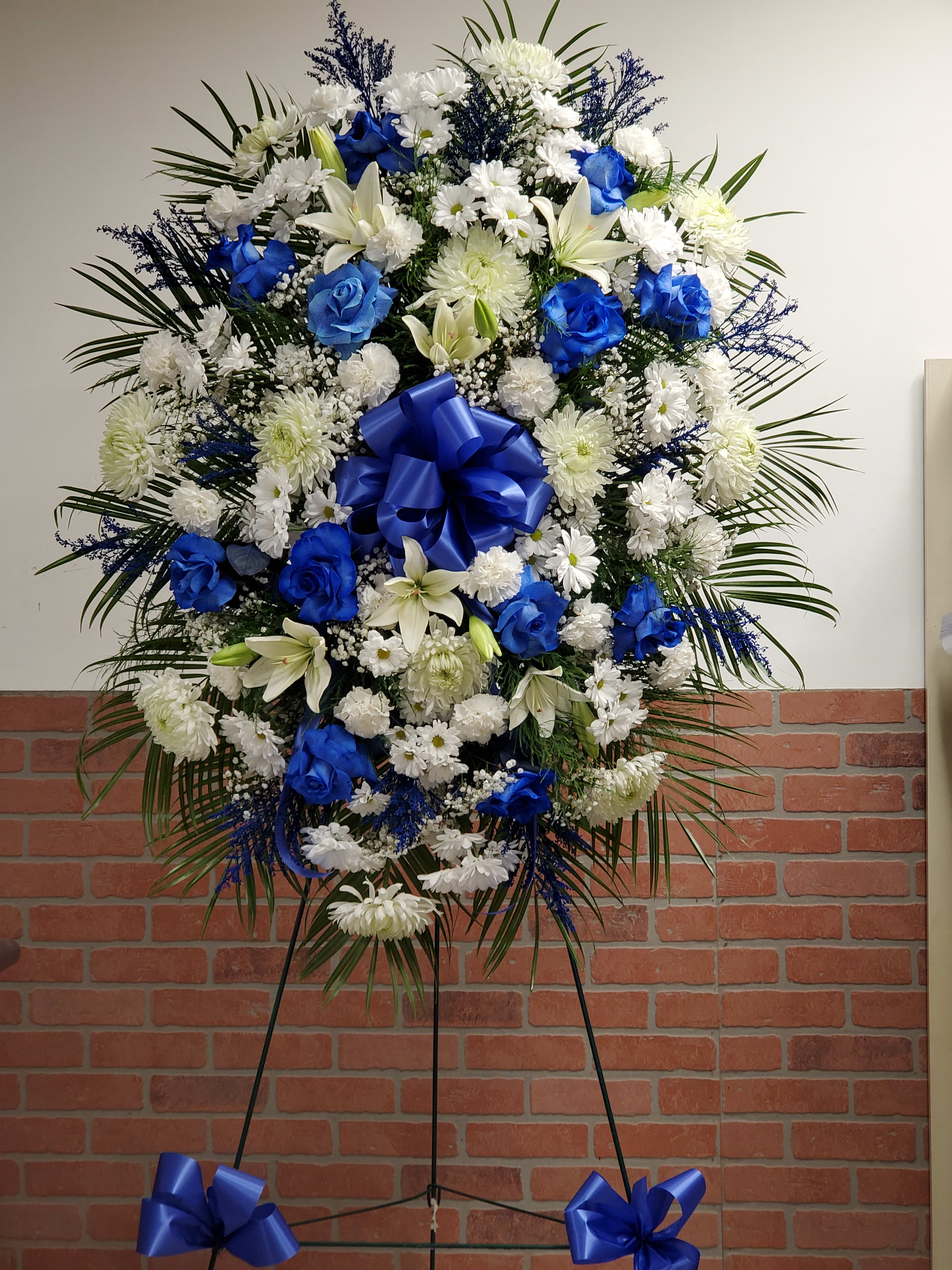 Large blue and white standing spray with roses, lilies, and mums on an easel.