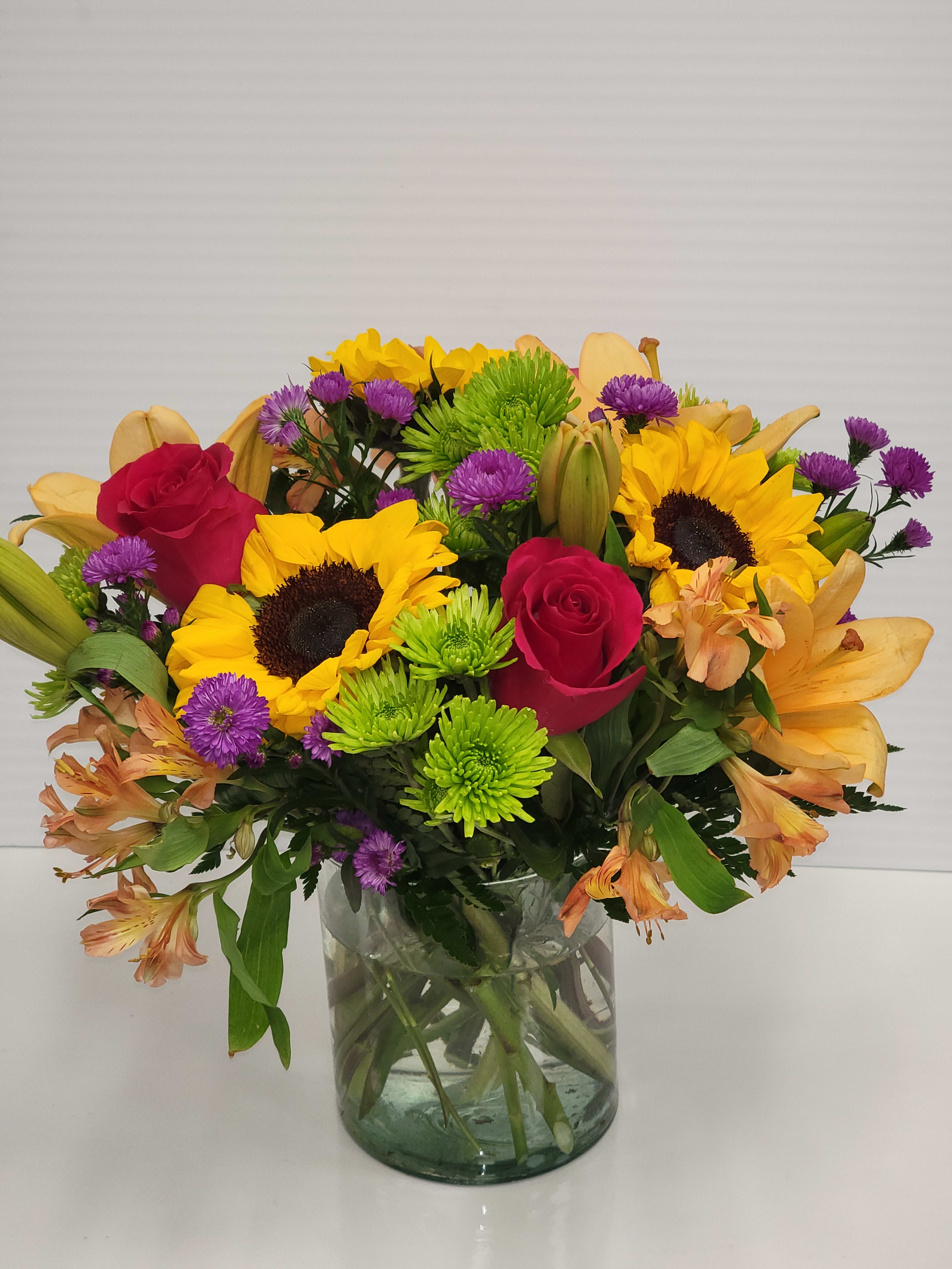Mixed bouquet of sunflowers, red roses, and purple flowers in a glass vase