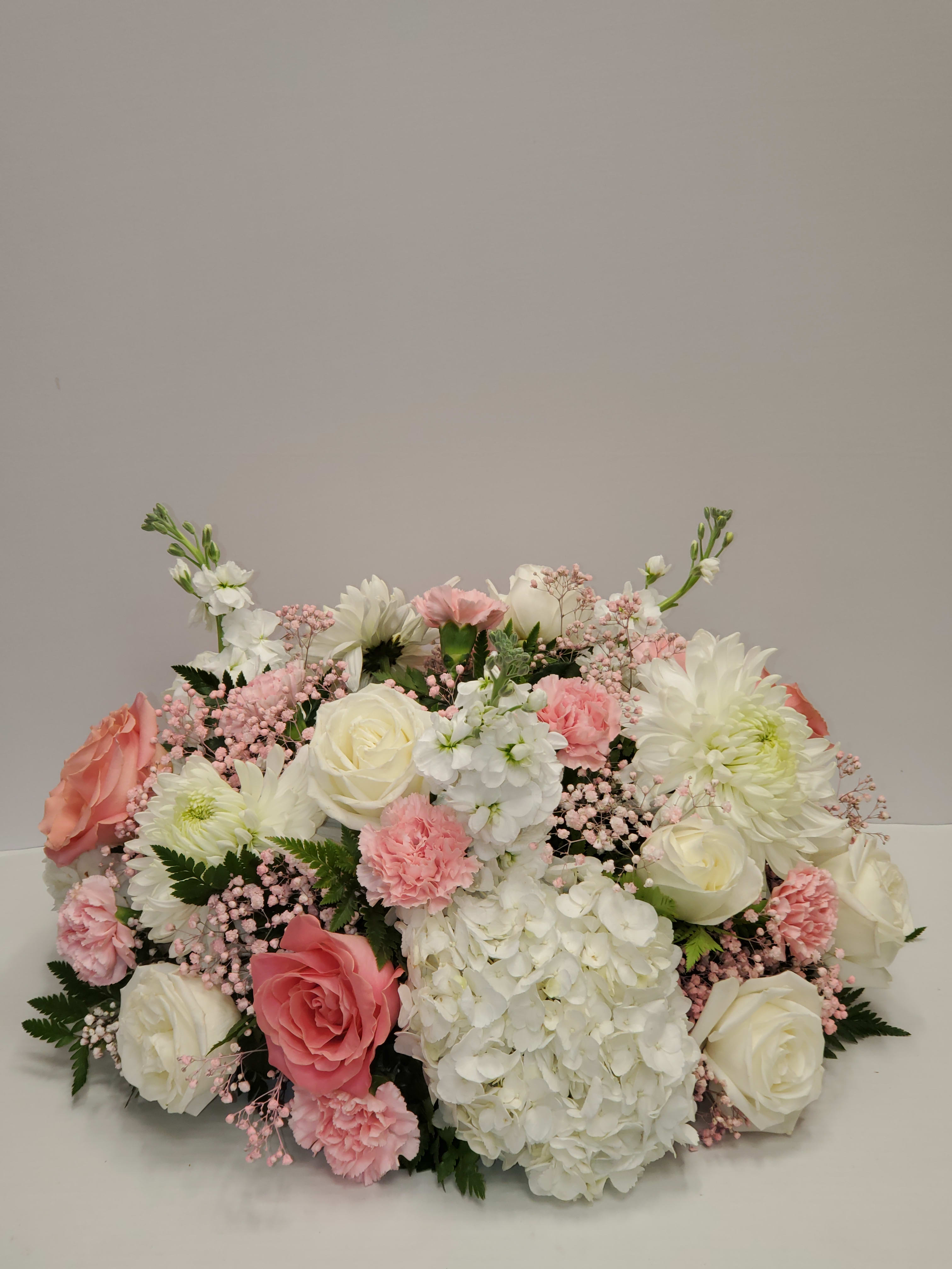Low centerpiece of white hydrangeas, roses, and pink carnations in a soft pastel palette