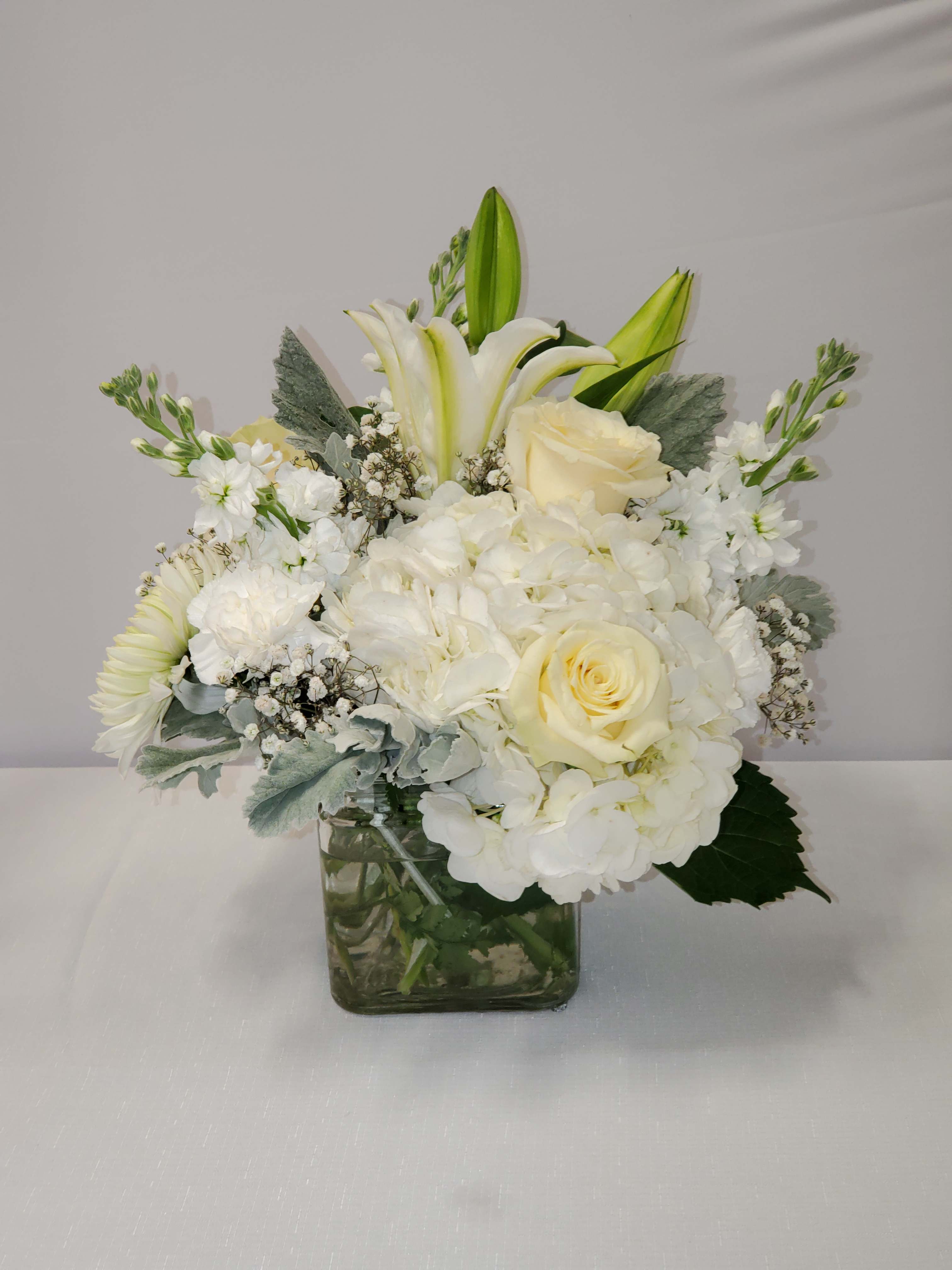 Compact white and ivory bouquet of roses, lilies, and hydrangeas in a clear glass cube vase