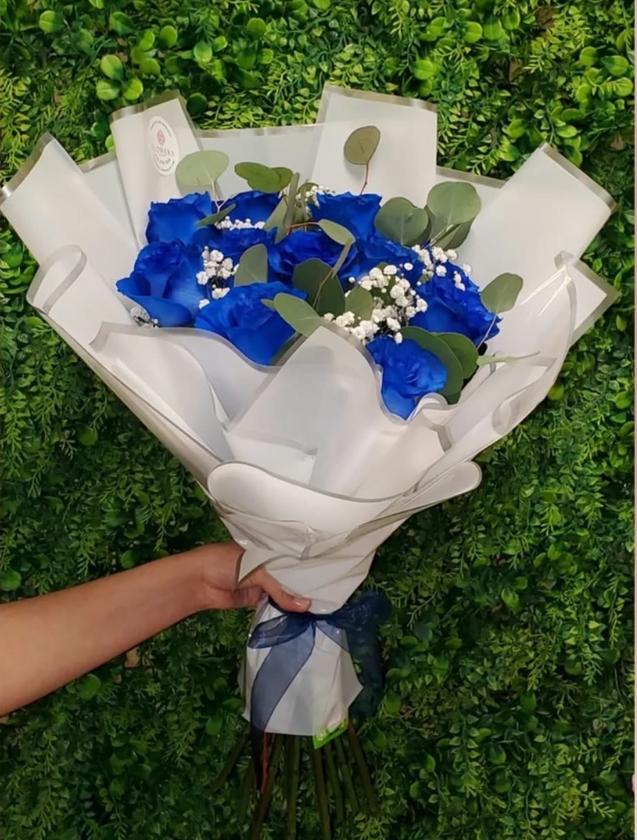 Handheld bouquet of vivid blue roses and white filler flowers wrapped in white paper