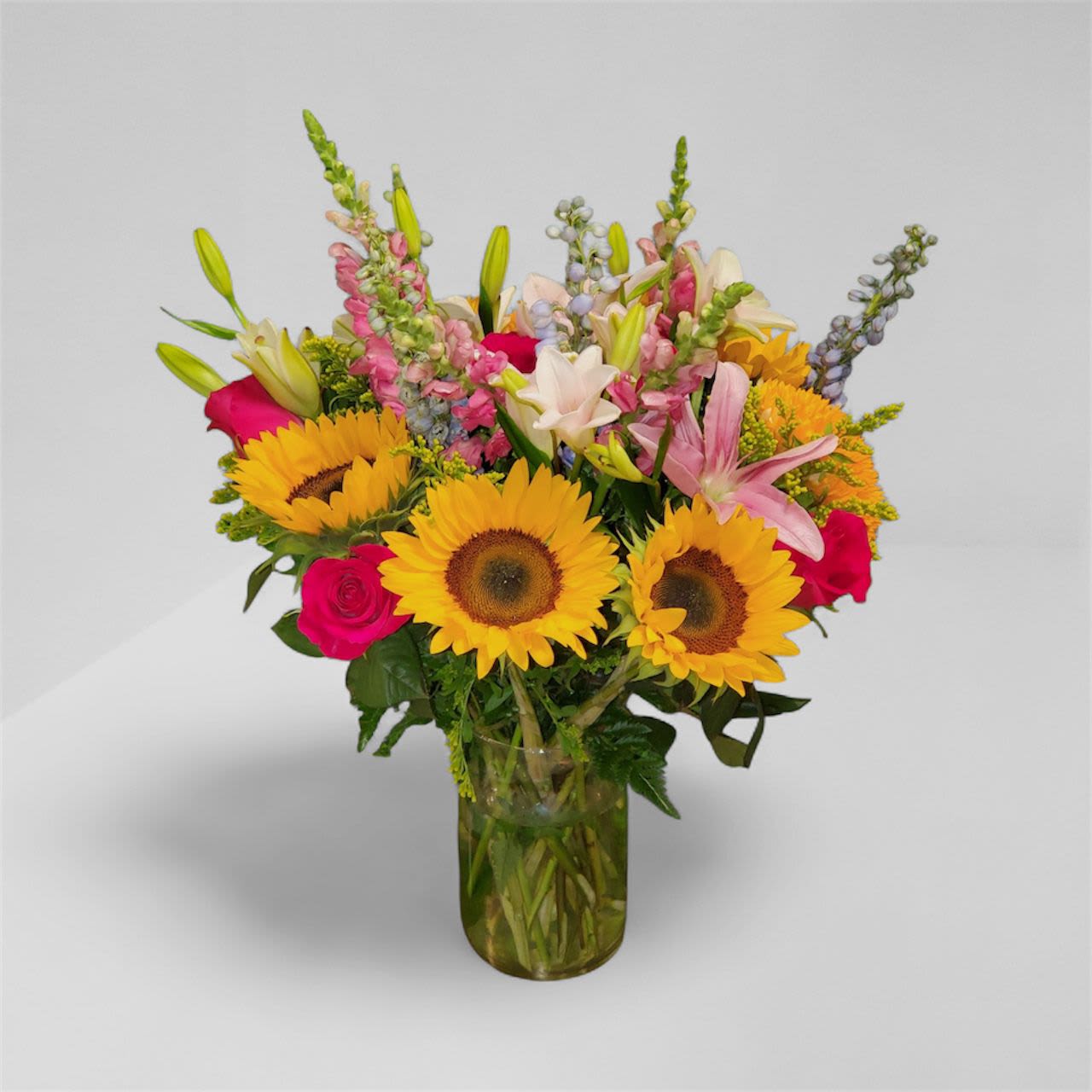 Bouquet of sunflowers, roses, lilies, and snapdragons in a glass vase