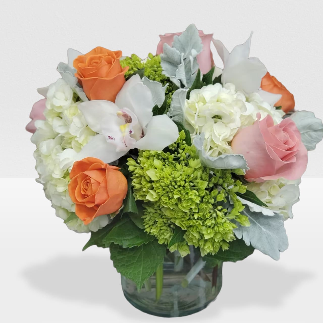 Round arrangement of orange and pink roses, white orchids and hydrangeas in a clear glass vase