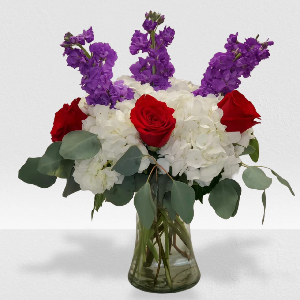 Love on First seeing - This vibrant bouquet will show that special someone how passionate you are about them. Love at First Sight by BloomNation™ is a great gift for Valentine's Day, a birthday, an anniversary, or a romantic gesture.    Arrangement Details: Includes white 3 hydrangea, 5 red roses, 4 purple stock, &amp; seeded eucalyptus.  APPROXIMATE DIMENSIONS: 13"H X 10" W