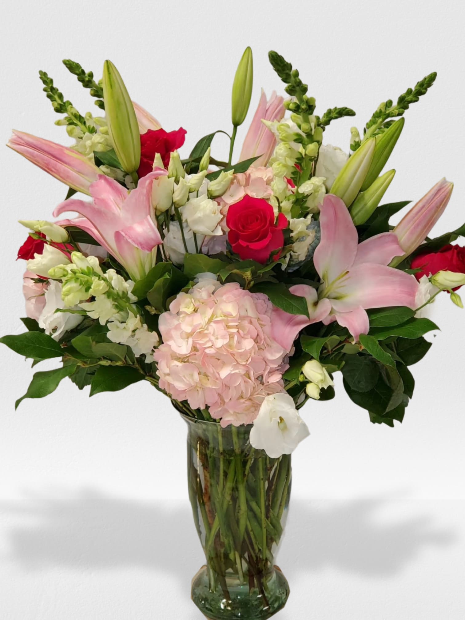 Tall arrangement of pink lilies, red roses, and white flowers in a clear glass vase
