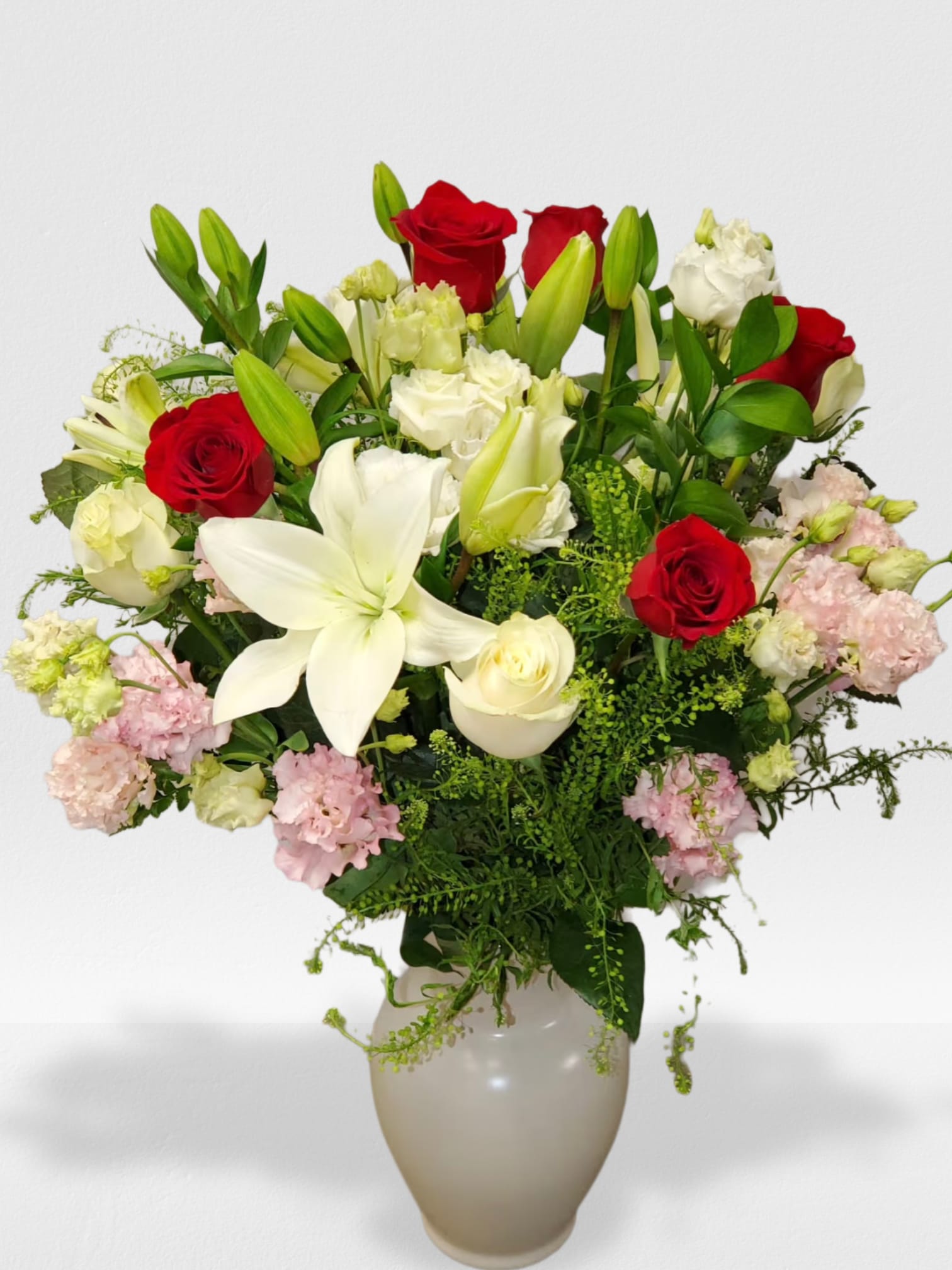 Tall arrangement of red roses, white lilies, and mixed pastel blooms in a white vase