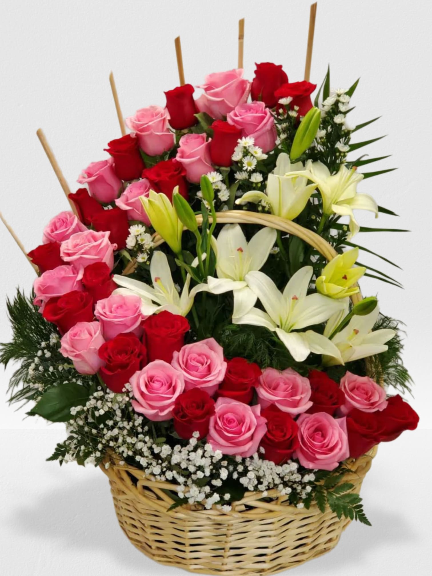 Basket arrangement of pink and red roses with white lilies and small white filler flowers.