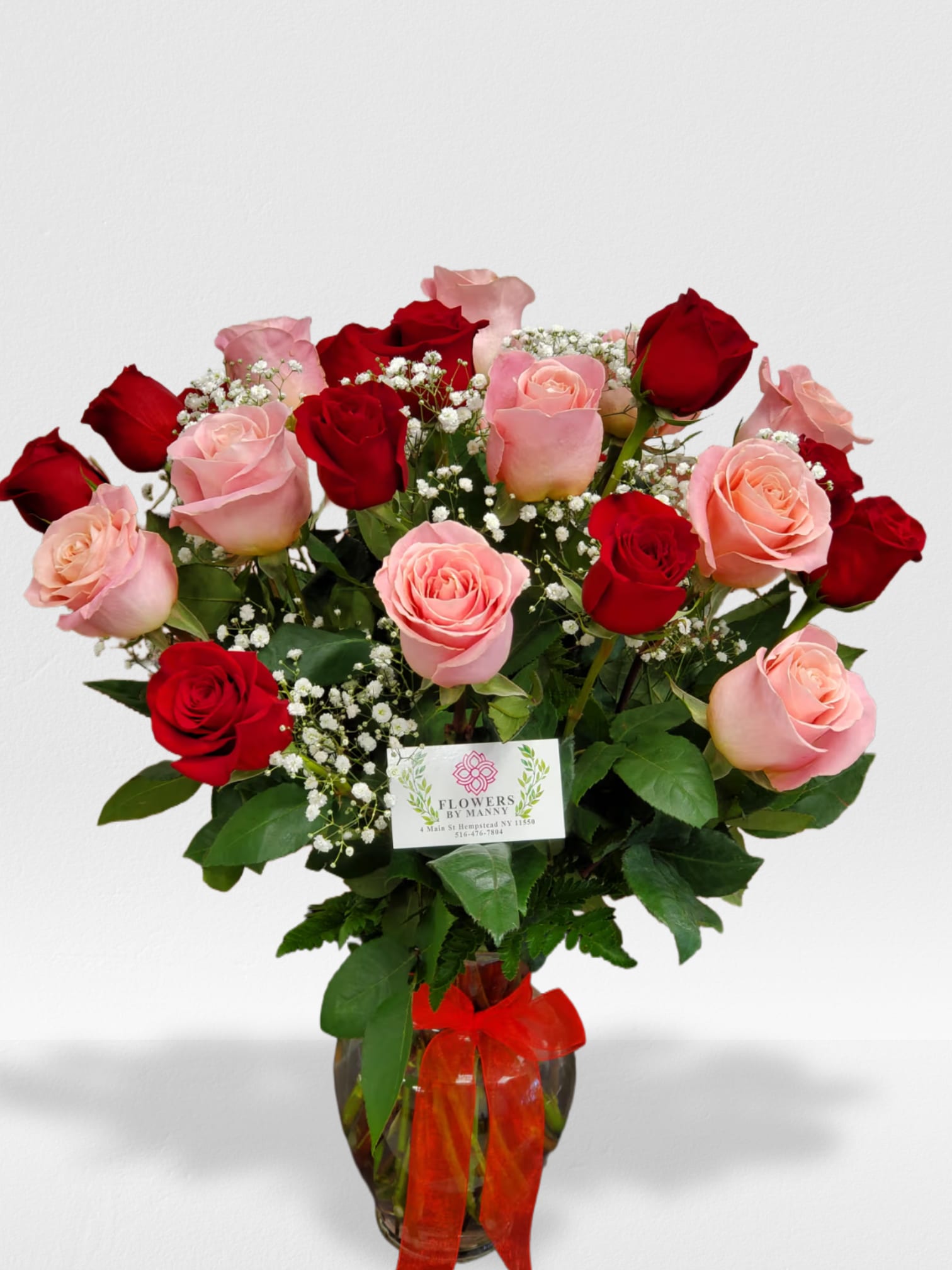 Arrangement of red and pink roses with white filler flowers in a glass vase with a red bow
