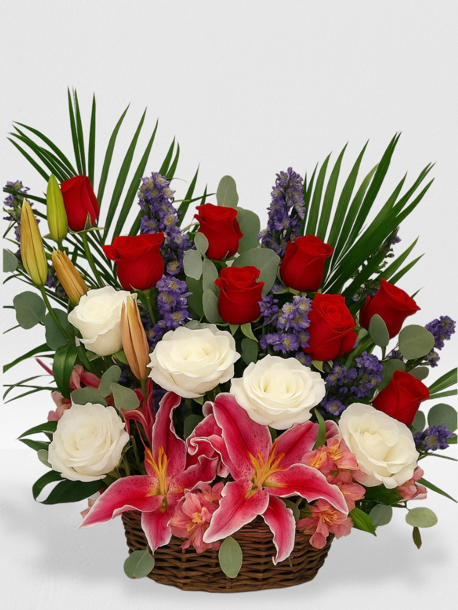 Basket arrangement of red and white roses with pink lilies and purple flowers.