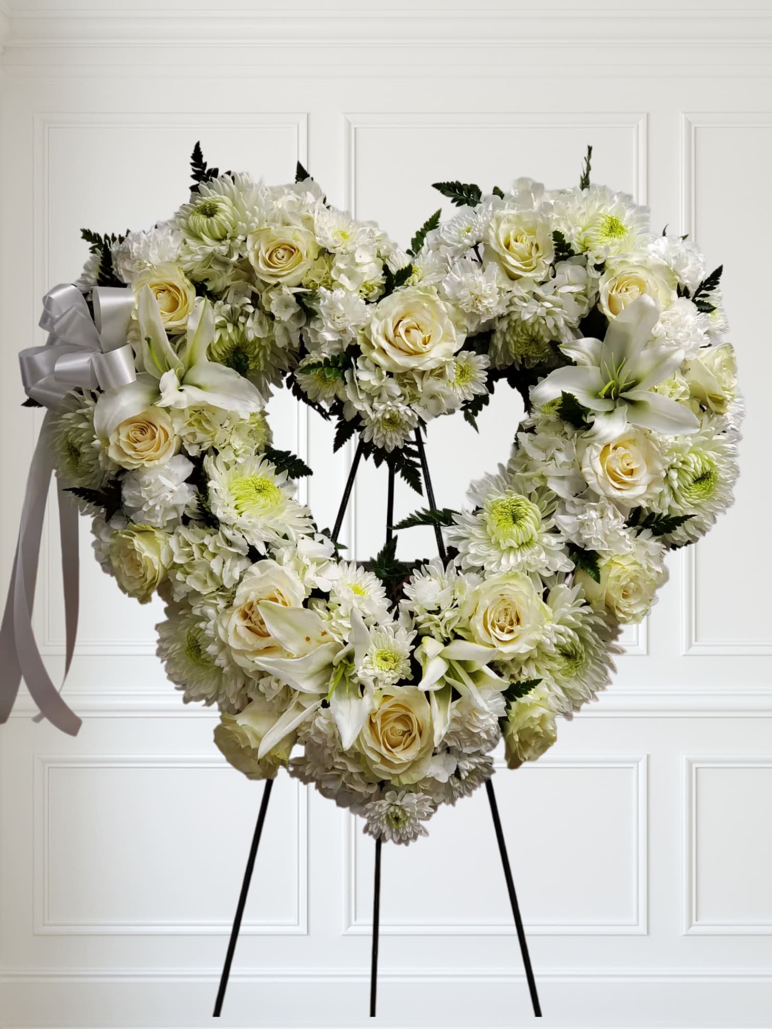 Love in our Hearts by Manny - An all white tribute, this heart shaped easel shows your everlasting love. Featuring a variety of white flowers and greenery, this heart with a trail of ivy compliments the beauty of life. 