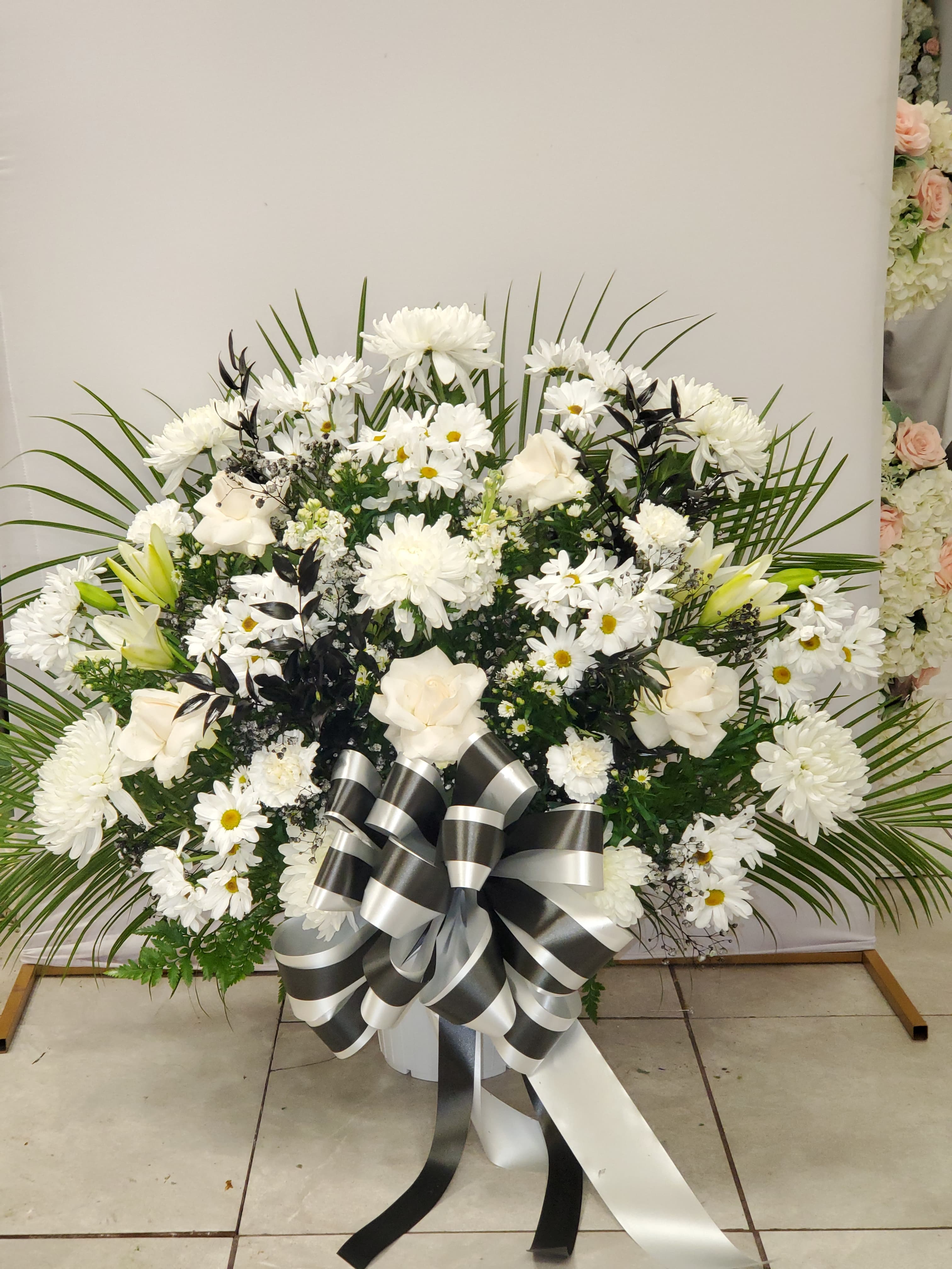 Large white floral spray with daisies, roses, and a black-and-white ribbon bow