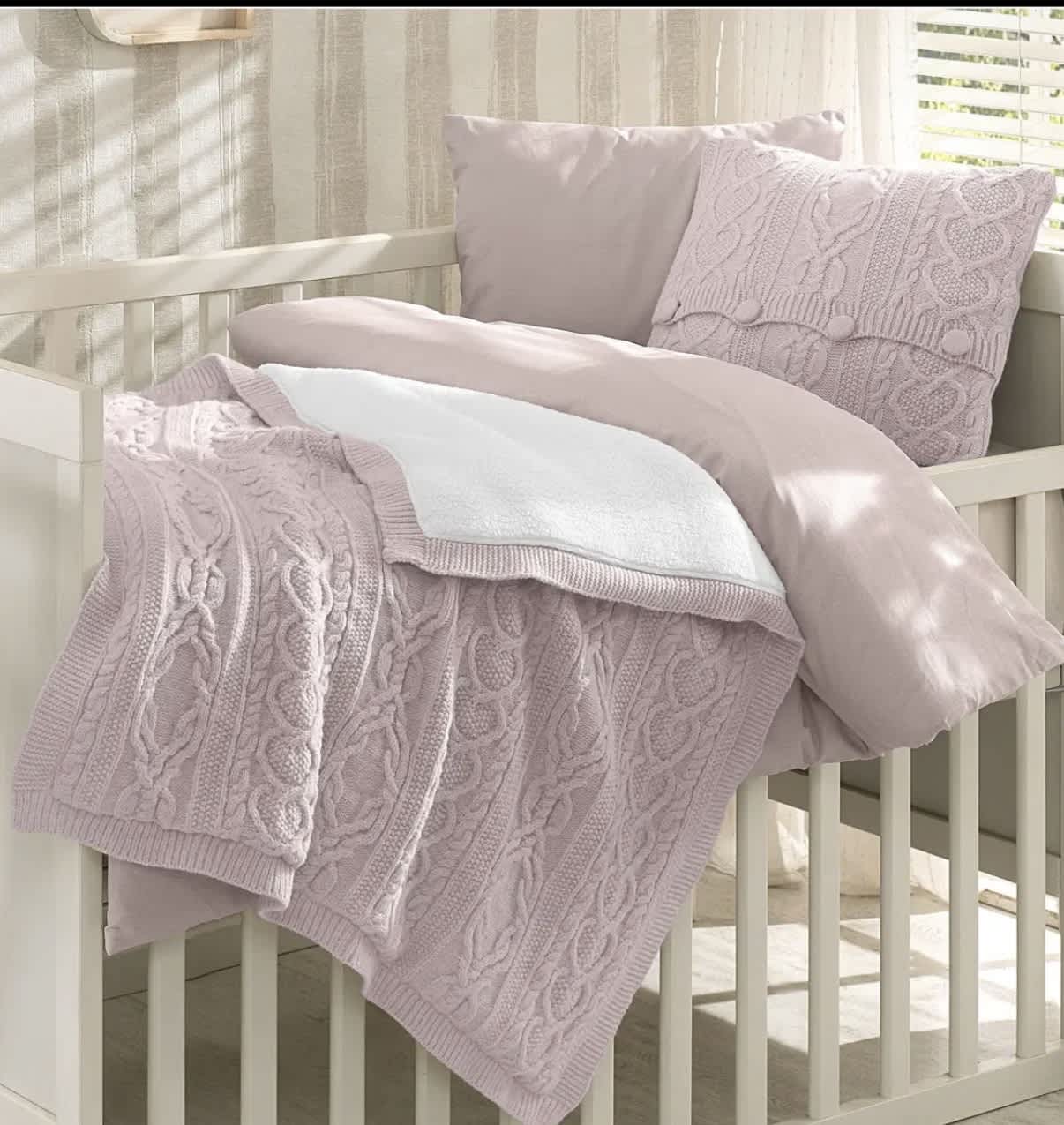 Pastel knit blanket and pillows arranged on a white crib
