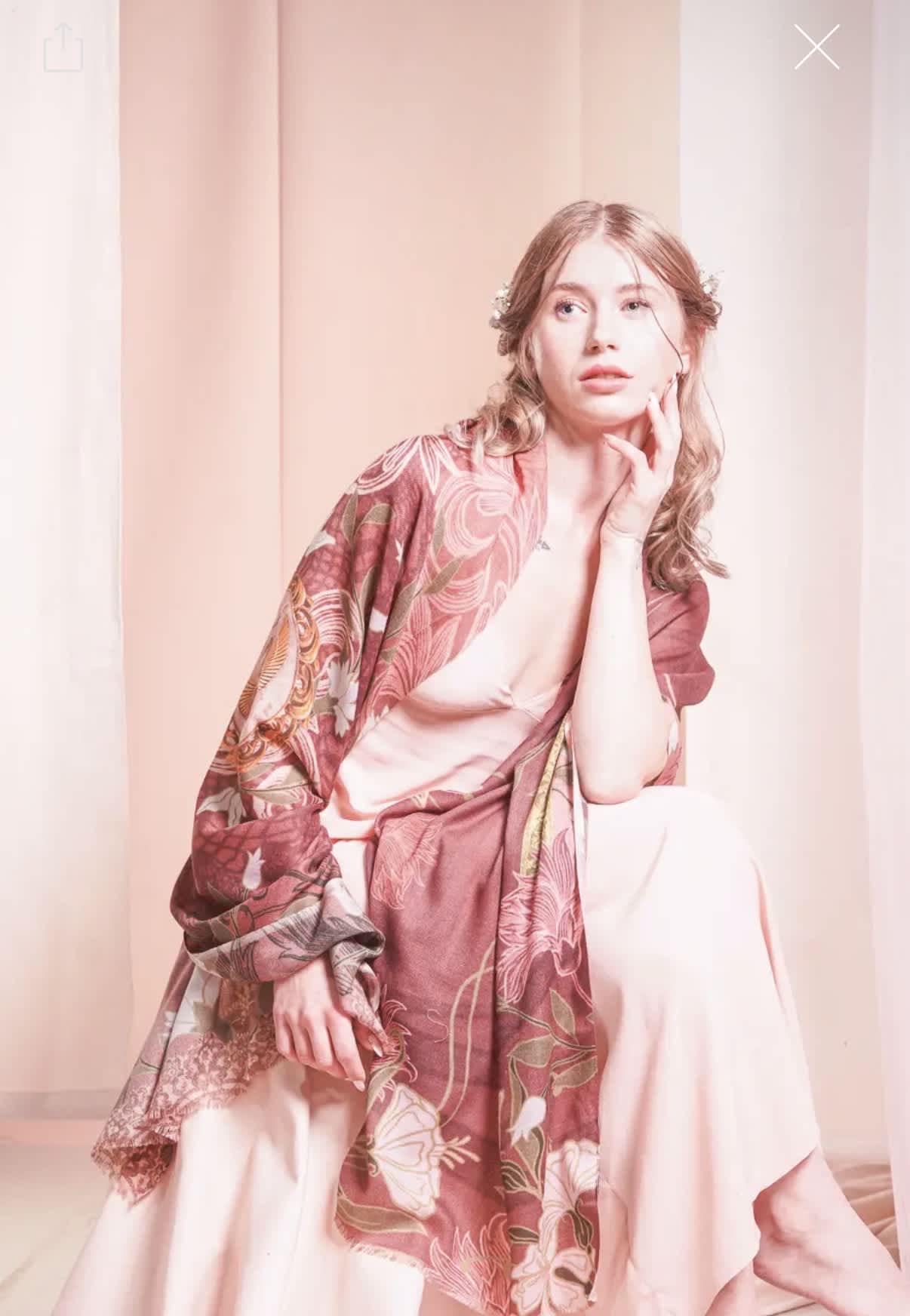 Woman wearing a pink floral shawl and pale dress against a soft pink backdrop
