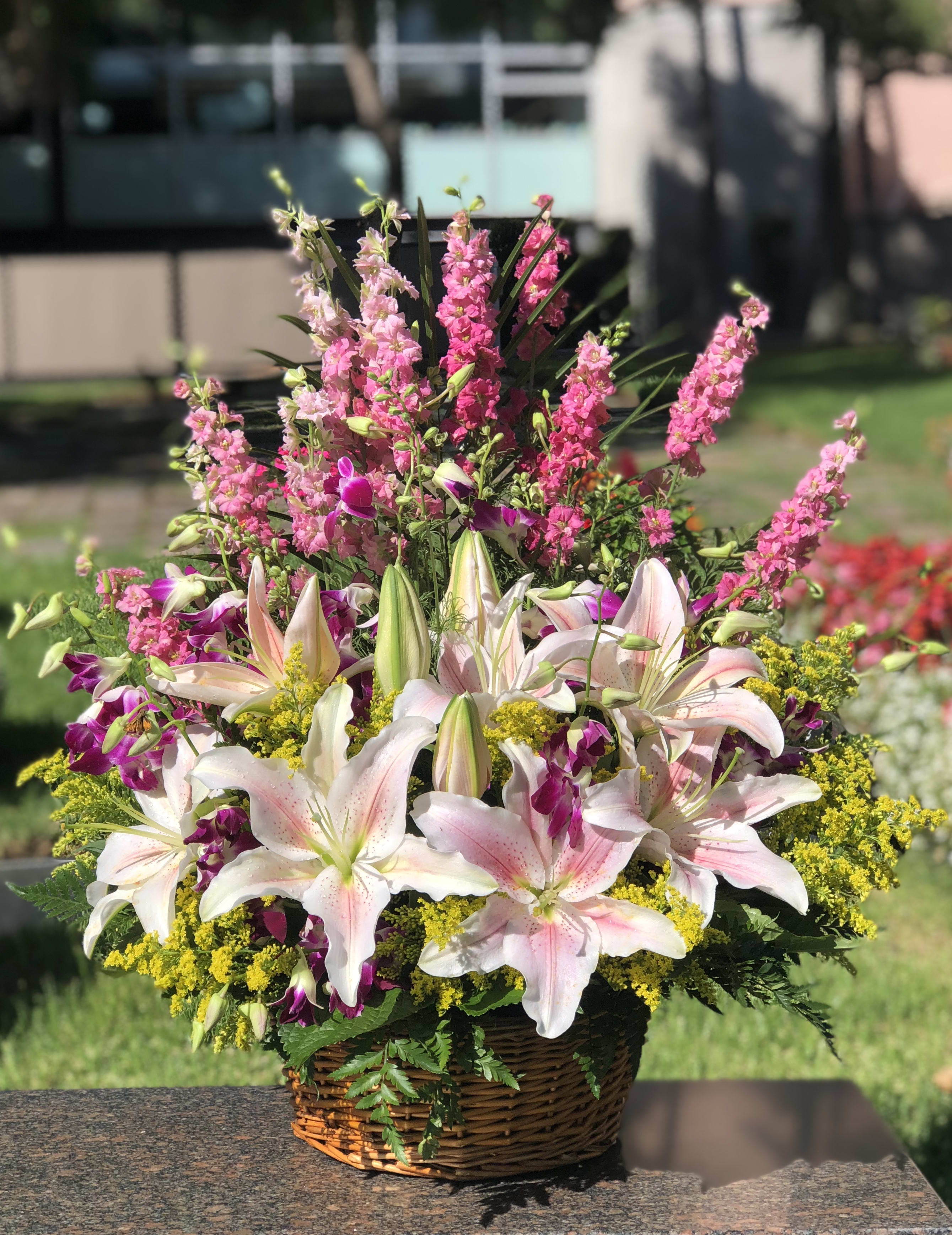 Basket arrangement of pink lilies, purple orchids, and yellow filler flowers