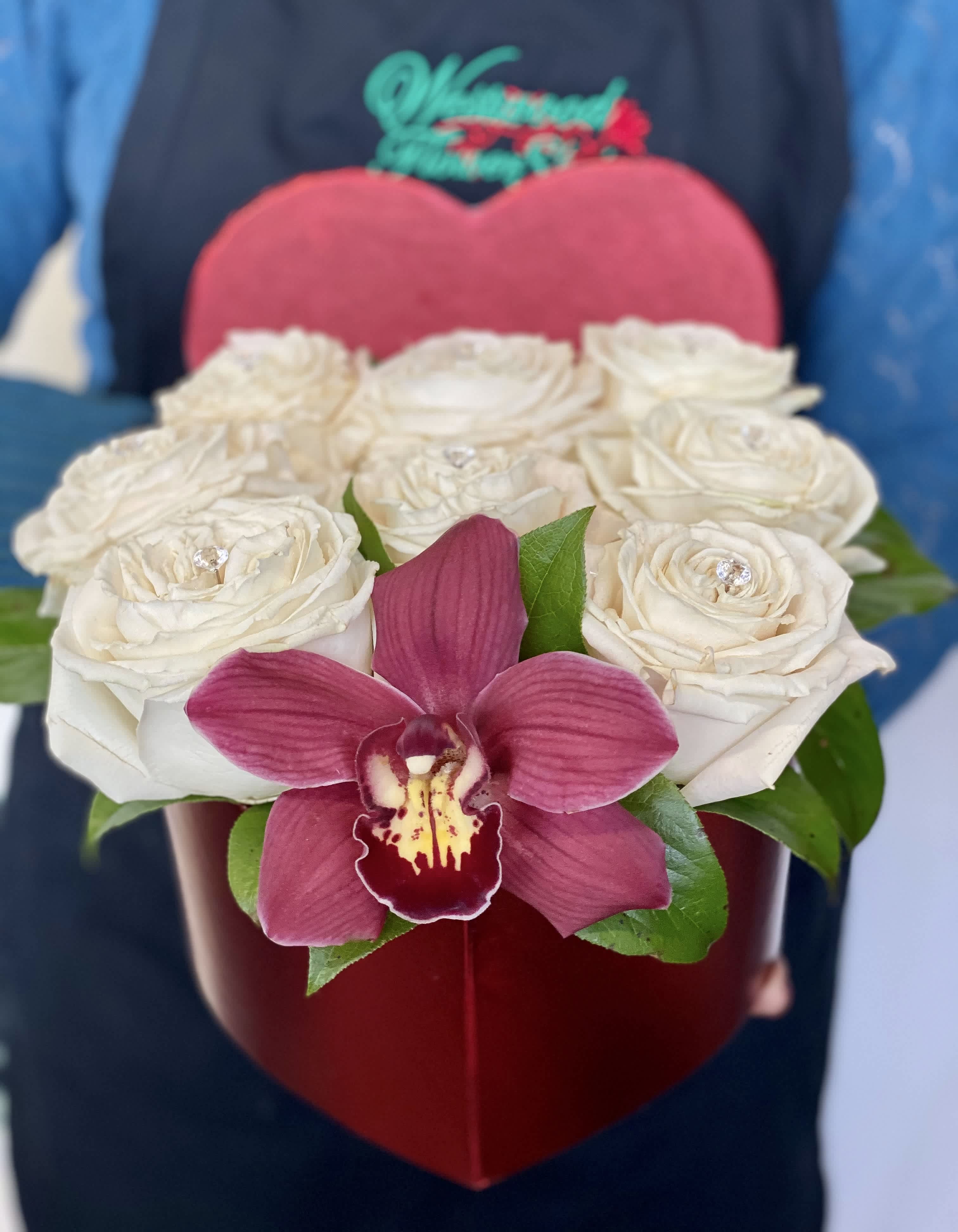 White roses in a red heart-shaped box with a pink orchid
