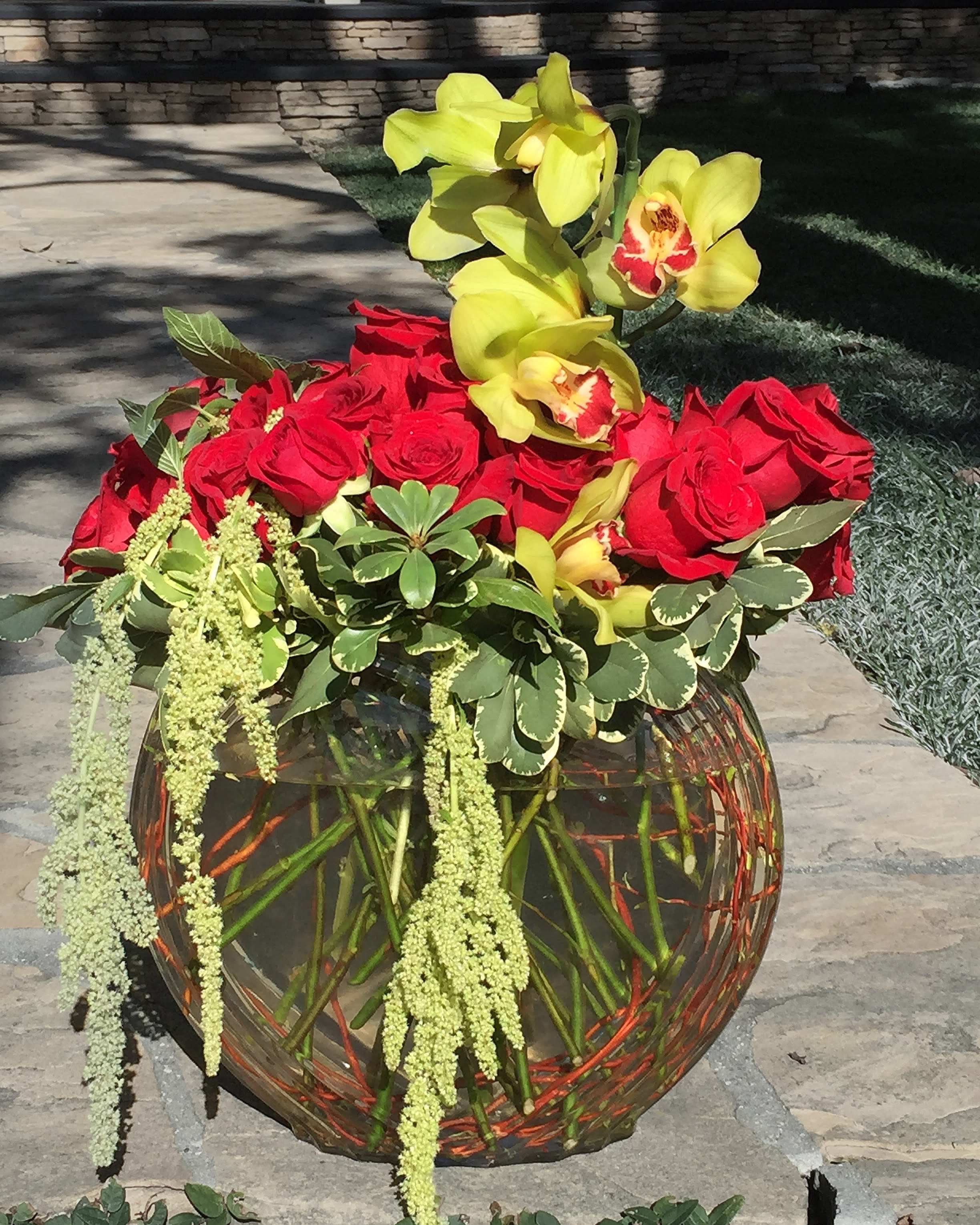 Red roses and yellow orchids in a round glass vase