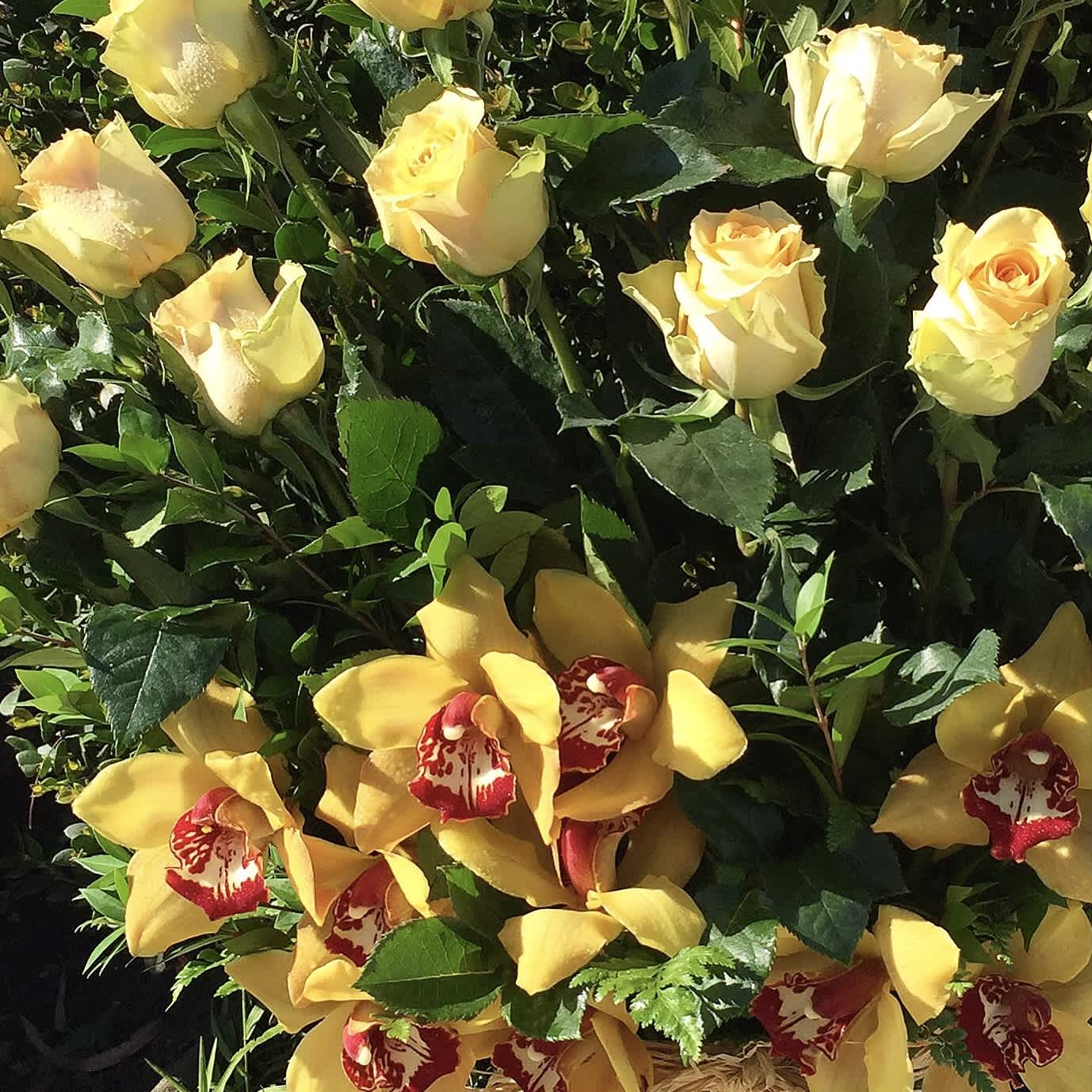Yellow roses and yellow orchids arranged with dark green foliage