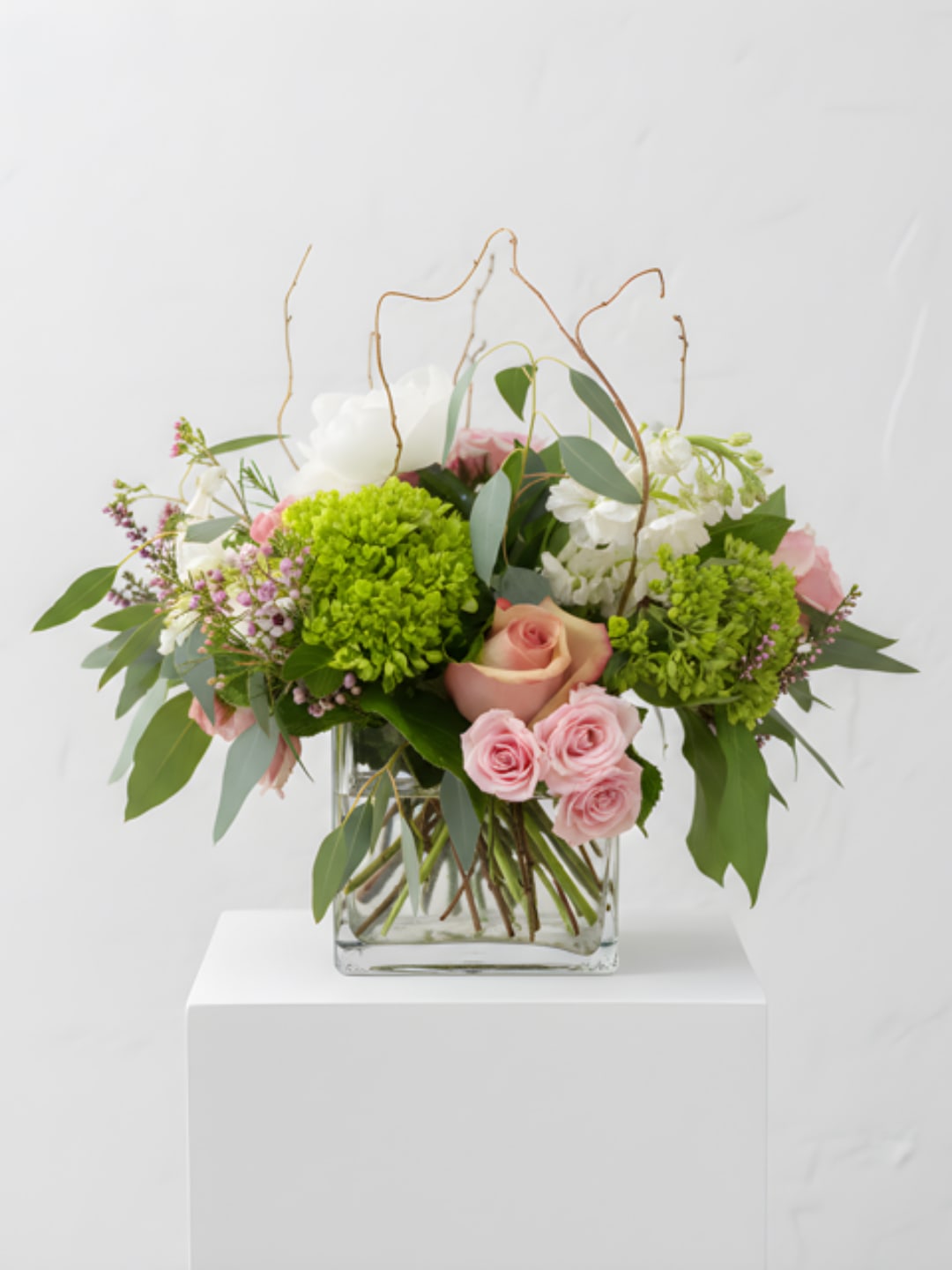 Pink roses and green blooms arranged in a clear glass vase