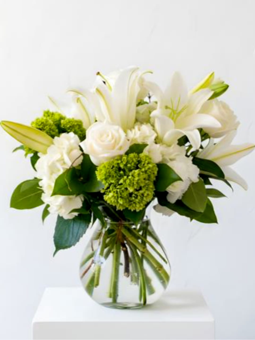 White lilies and roses in a clear glass vase with green accents