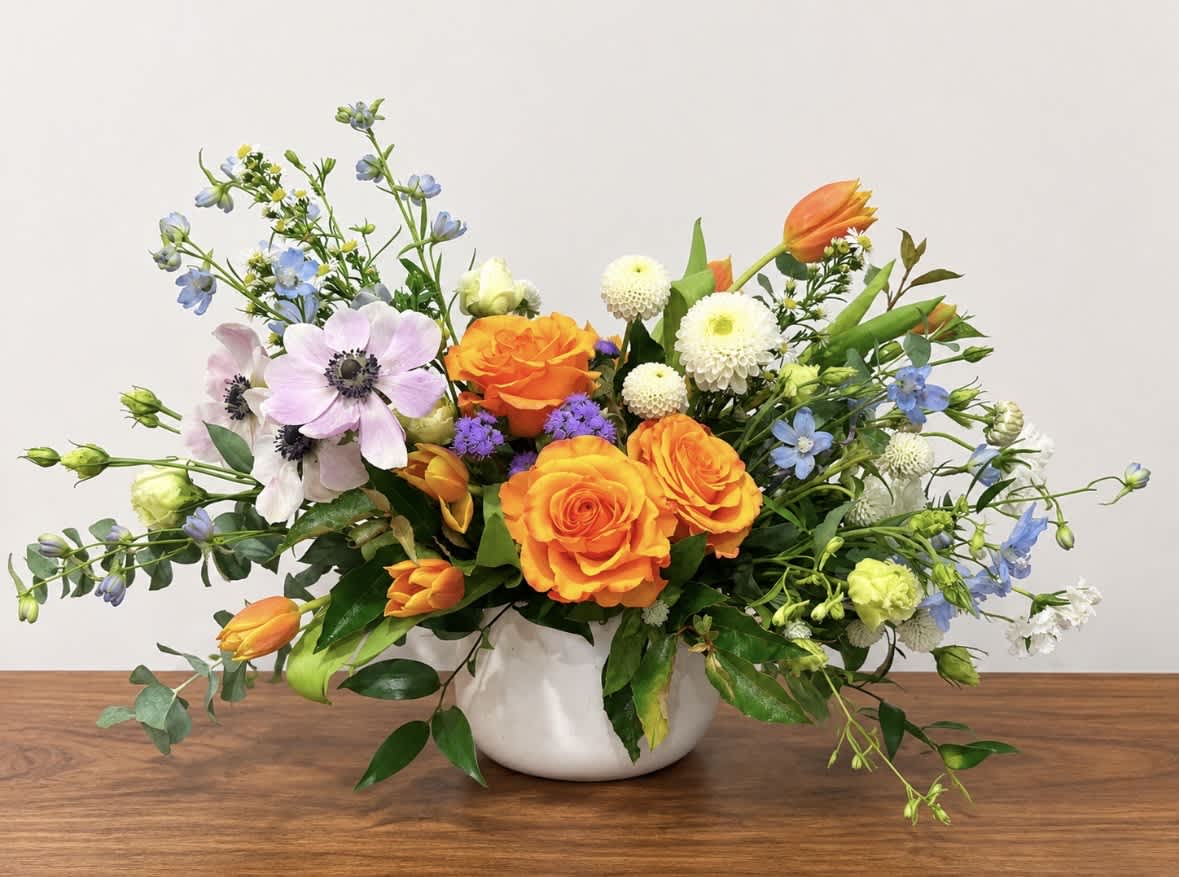 Mixed bouquet of orange roses, tulips, and pastel flowers in a white vase