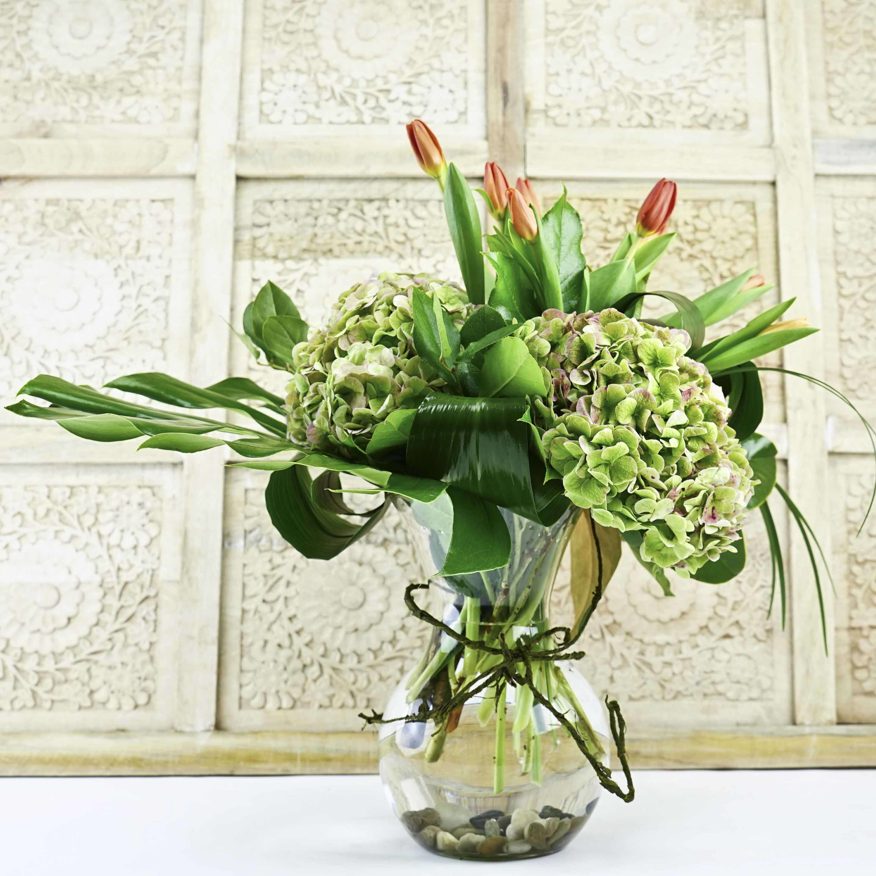 Bouquet of green hydrangeas and orange tulips in a glass vase