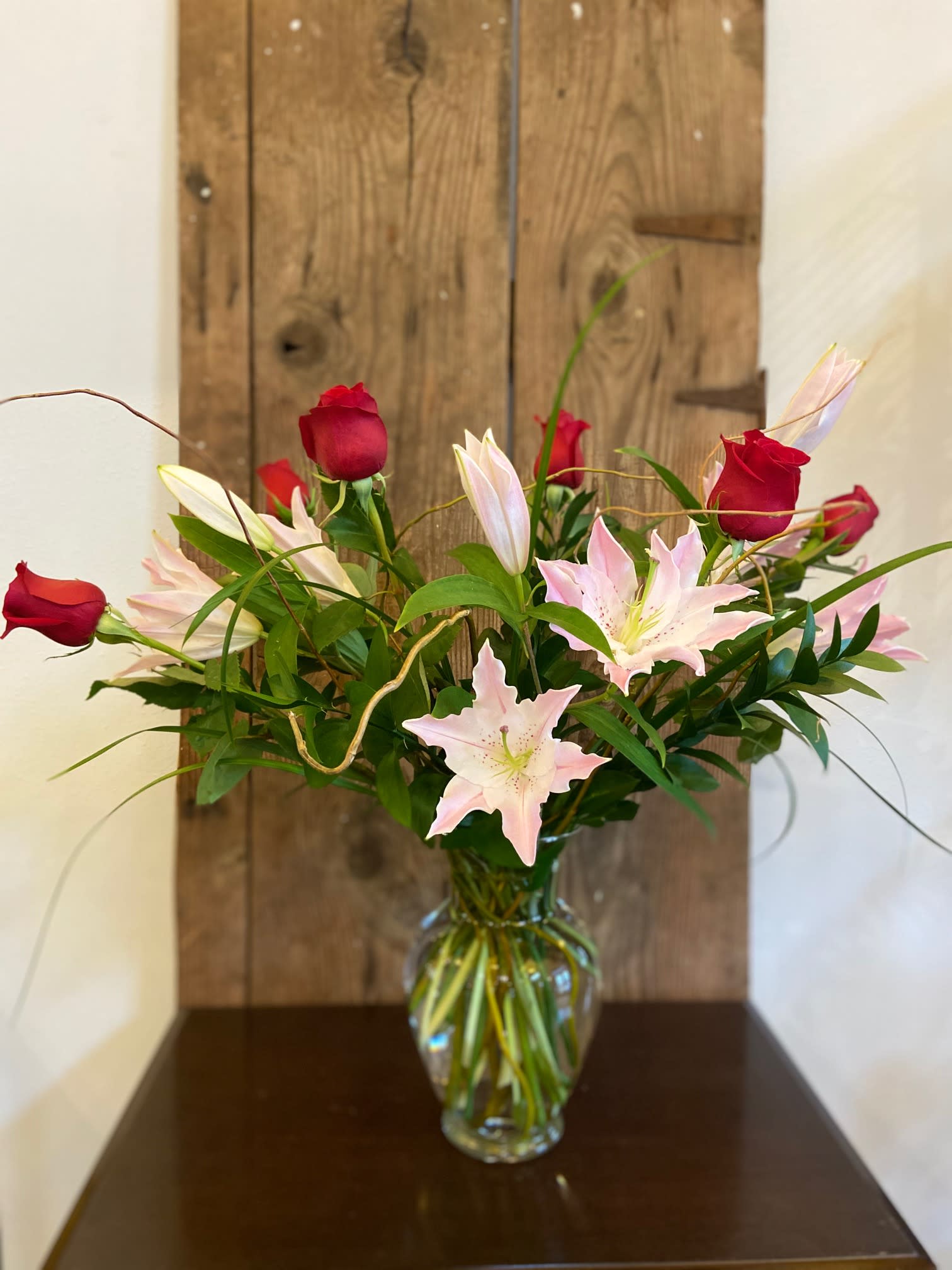 Tall arrangement of red roses and light pink lilies in a clear glass vase