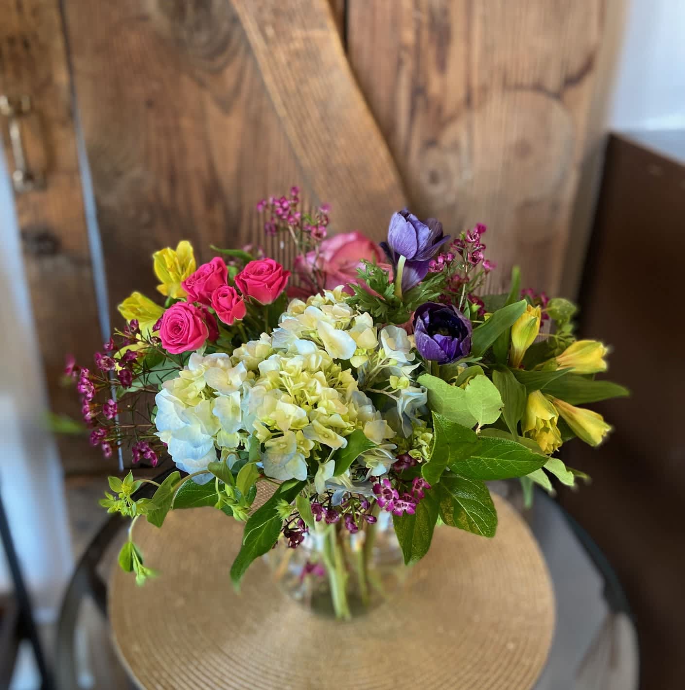 Mixed bouquet of white hydrangeas, pink spray roses, yellow alstroemeria and purple blooms in a glass vase