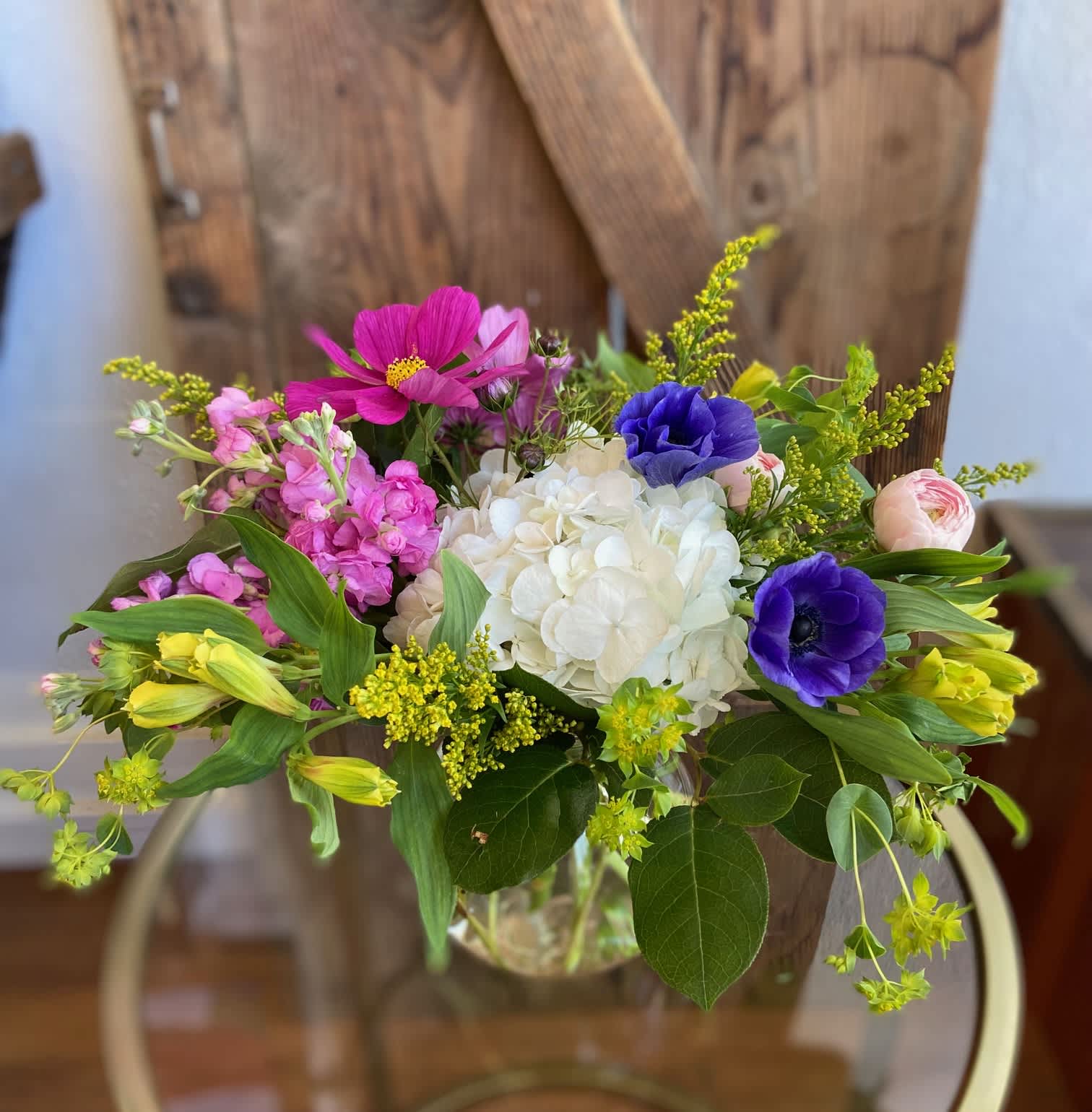 Colorful mixed bouquet with white hydrangea, purple anemones, and pink blooms in a clear glass vase