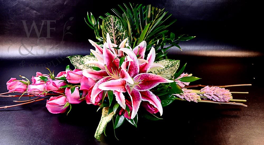 Pink roses and stargazer lilies arranged with greenery on a dark surface.