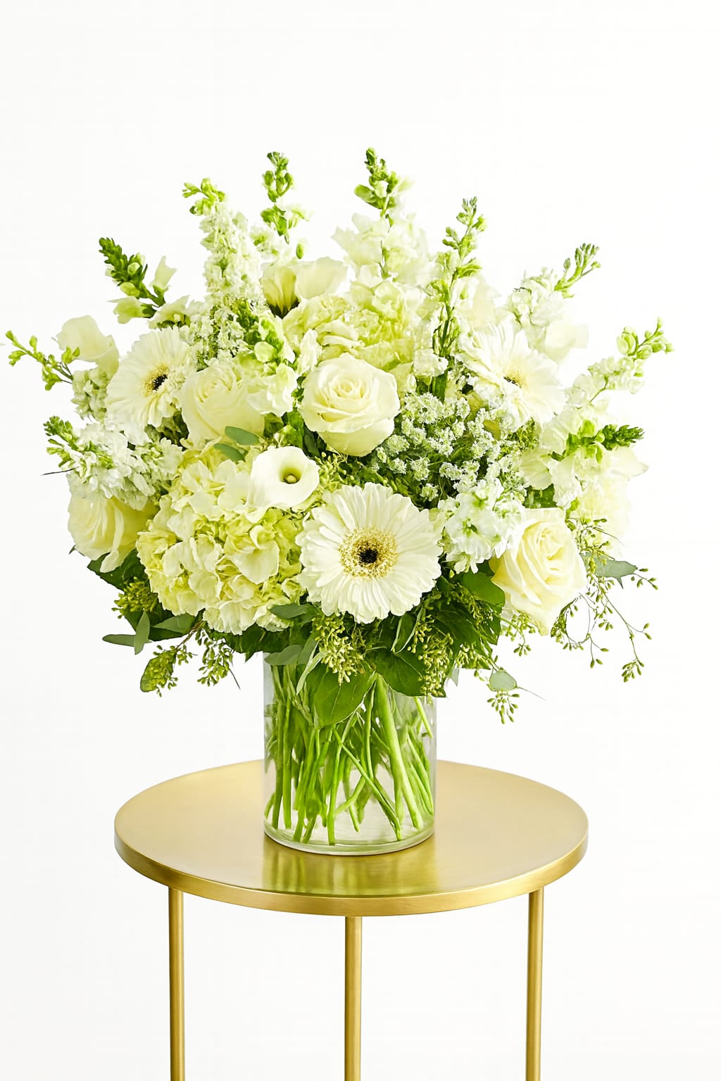 White floral arrangement in a clear glass vase on a gold table