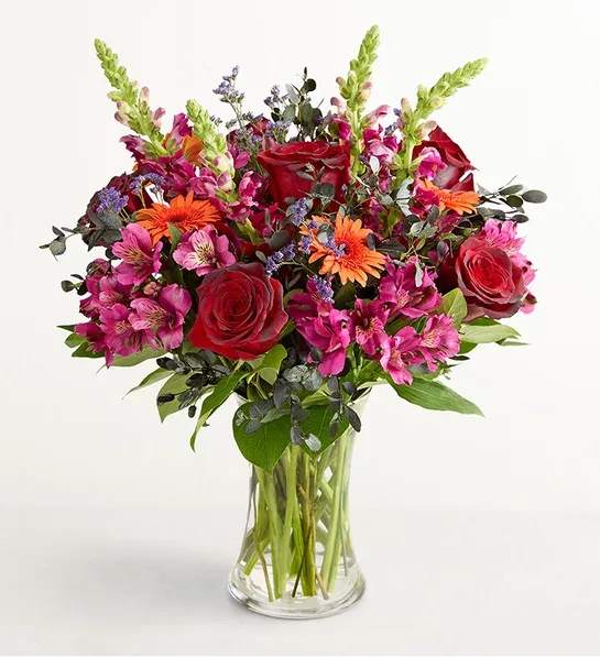 Bouquet of red roses, pink alstroemeria, and orange daisies in a clear glass vase