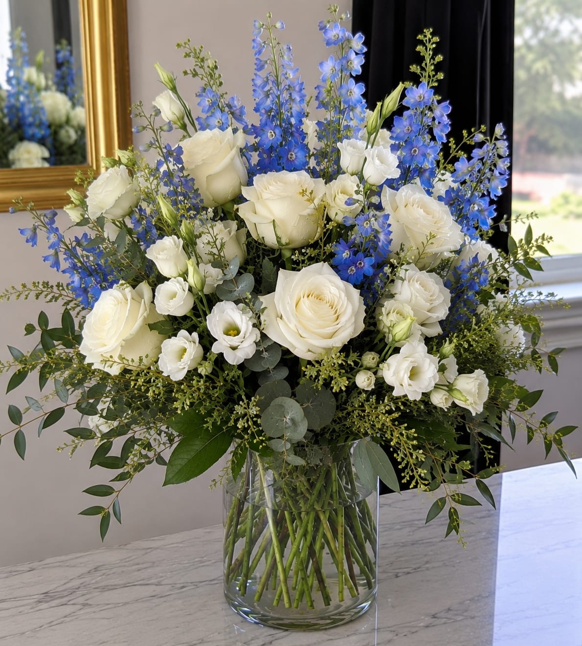 White roses and blue delphinium in a clear glass vase