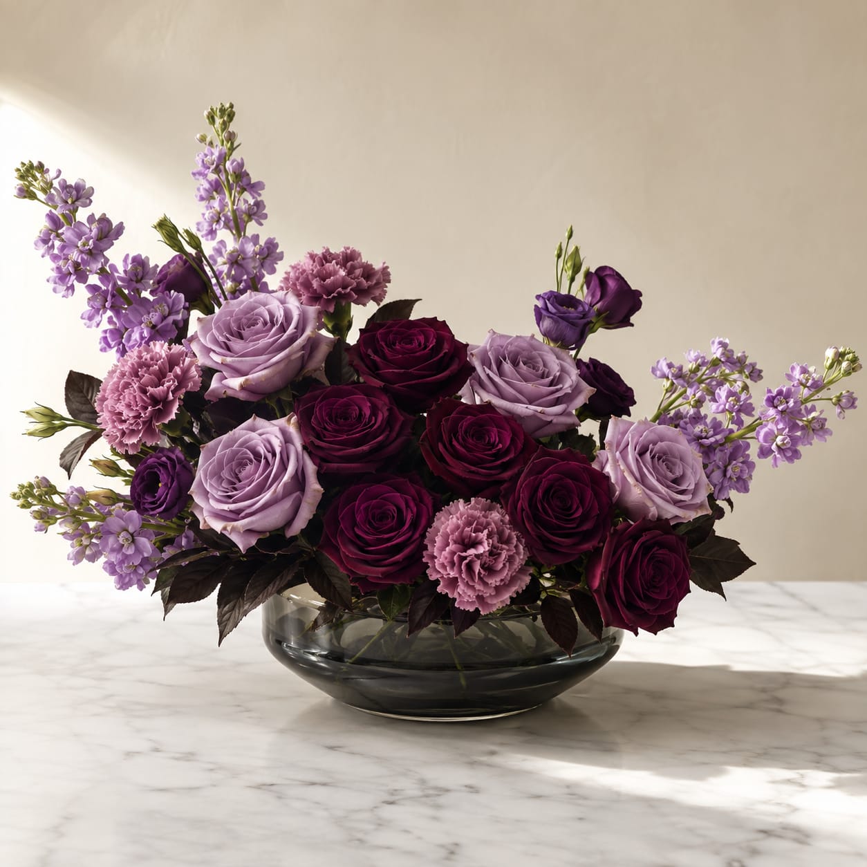 Purple and lavender roses with pink carnations in a glass bowl vase