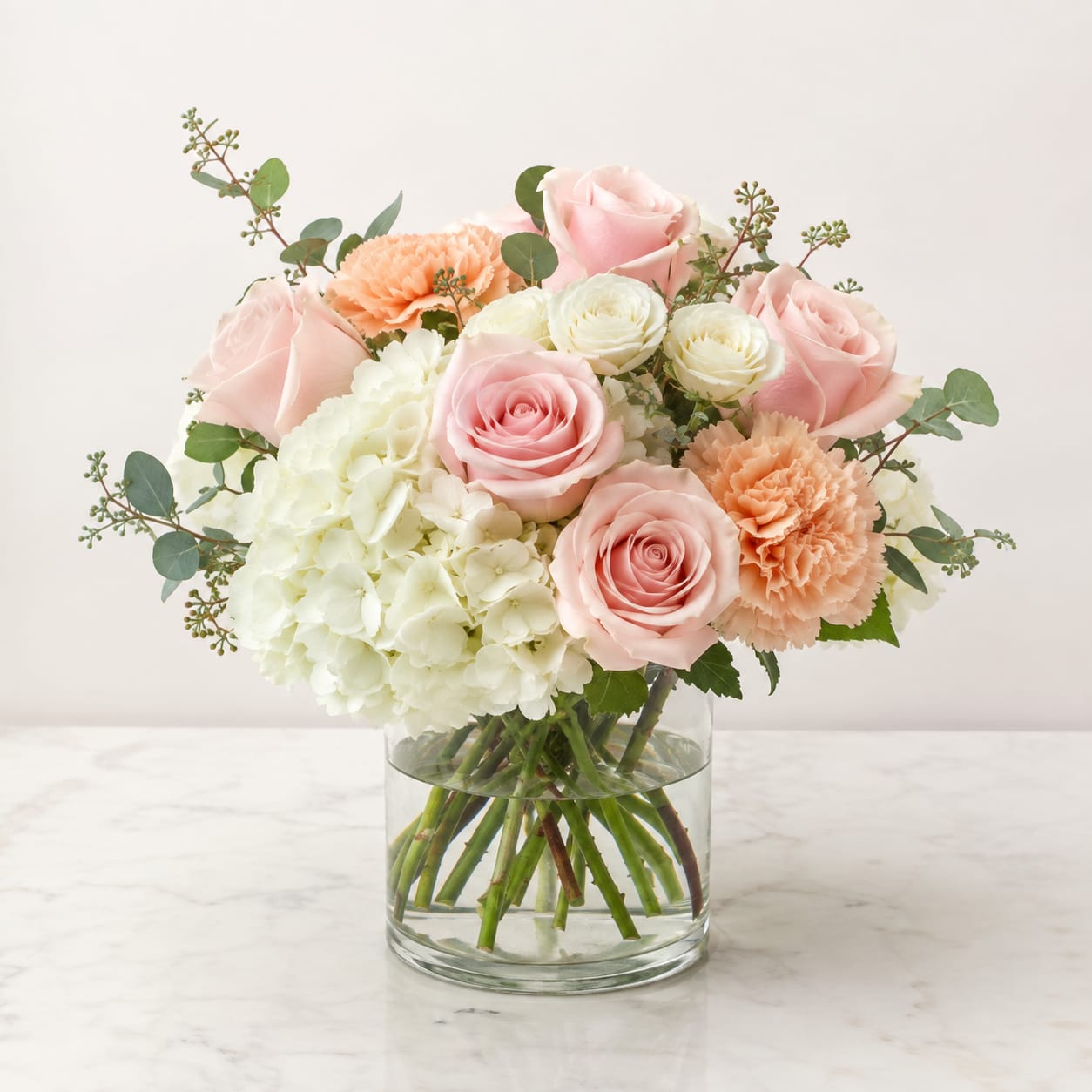 Pink roses, white hydrangea, and peach carnations in a clear glass vase