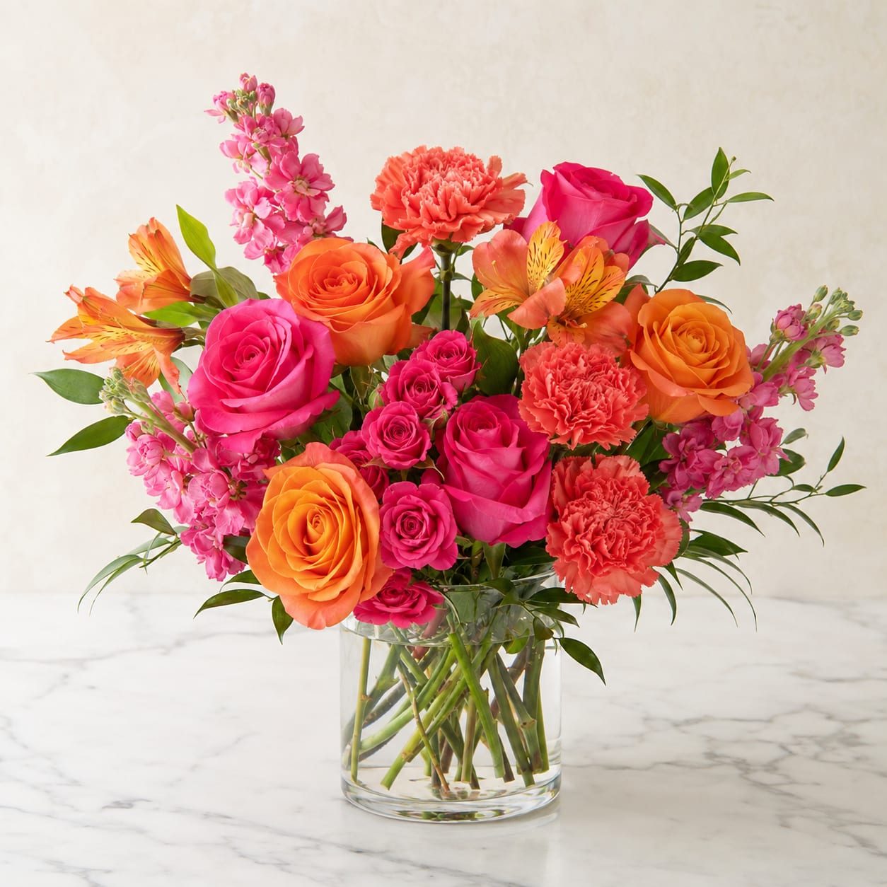 Bouquet of pink and orange roses, carnations, and alstroemeria in a clear glass vase