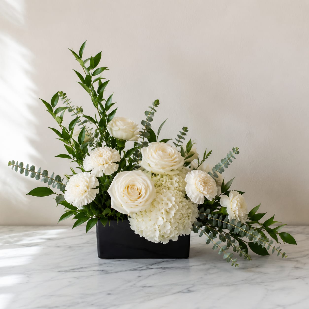 White roses and carnations arranged in a black rectangular vase