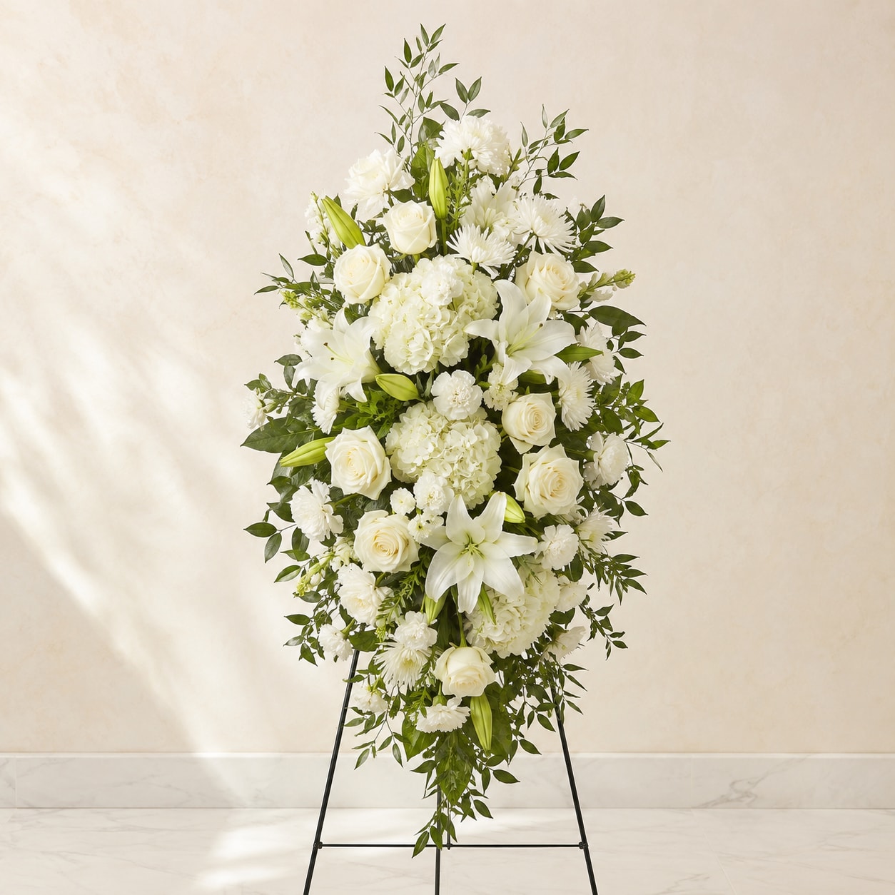 White funeral spray on a standing easel with lilies, roses, and hydrangeas