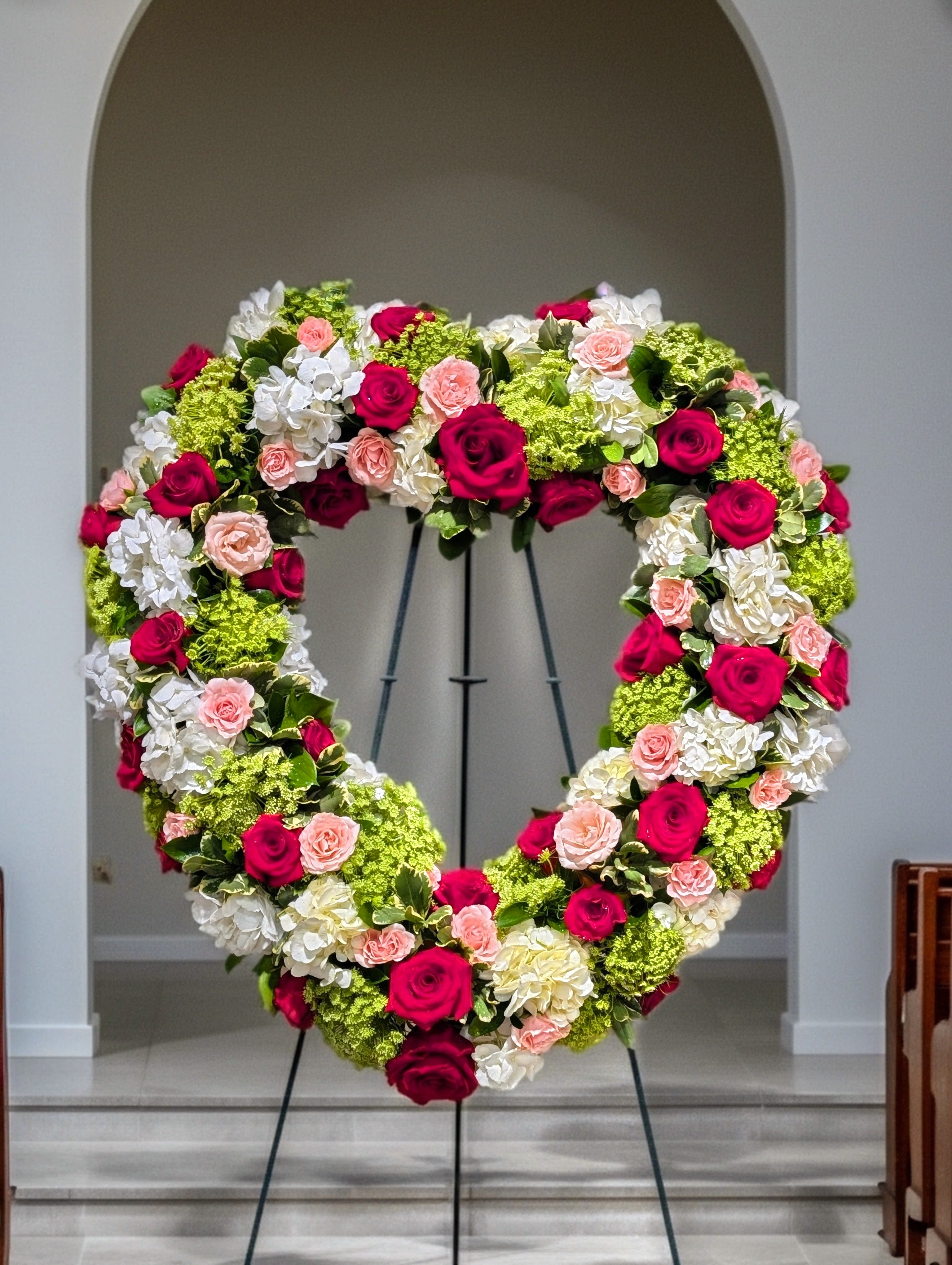 Condolences From The Heart – Hot Pink Rose &amp; Hydrangea Standing Wreath - Bouquet will be delivered approximately as pictured. A beautiful 24" open heart of red roses, pink spray roses, hydrangeas, seasonal fillers. Easel included.