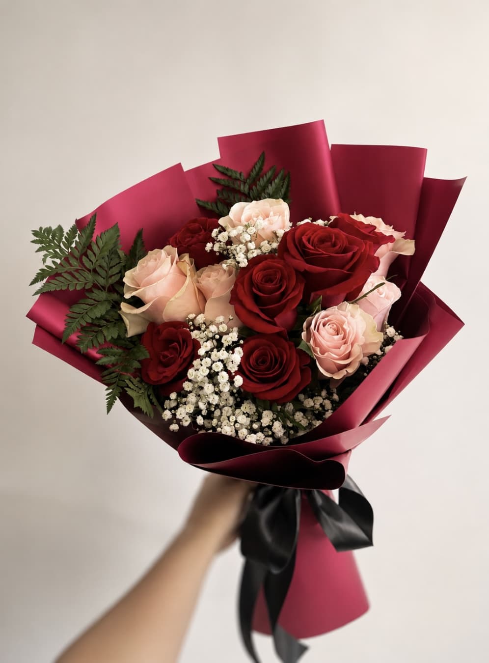Handheld bouquet of red and blush roses wrapped in burgundy paper