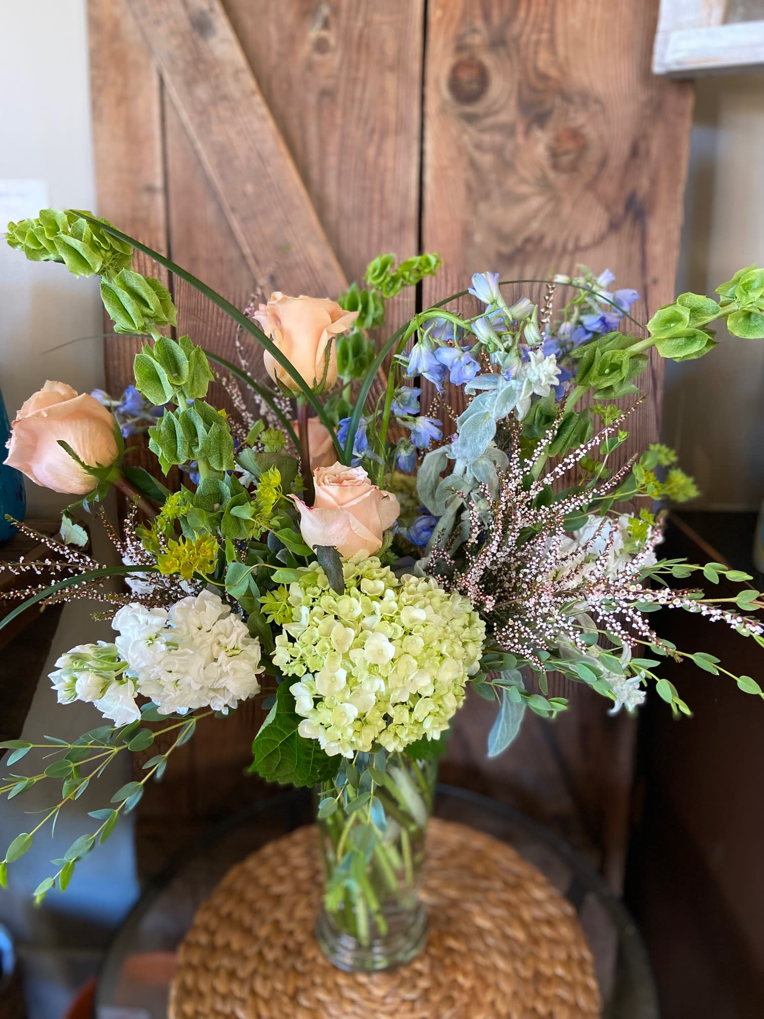 Tall vase arrangement with peach roses, green hydrangeas, bells of Ireland, and mixed accent flowers