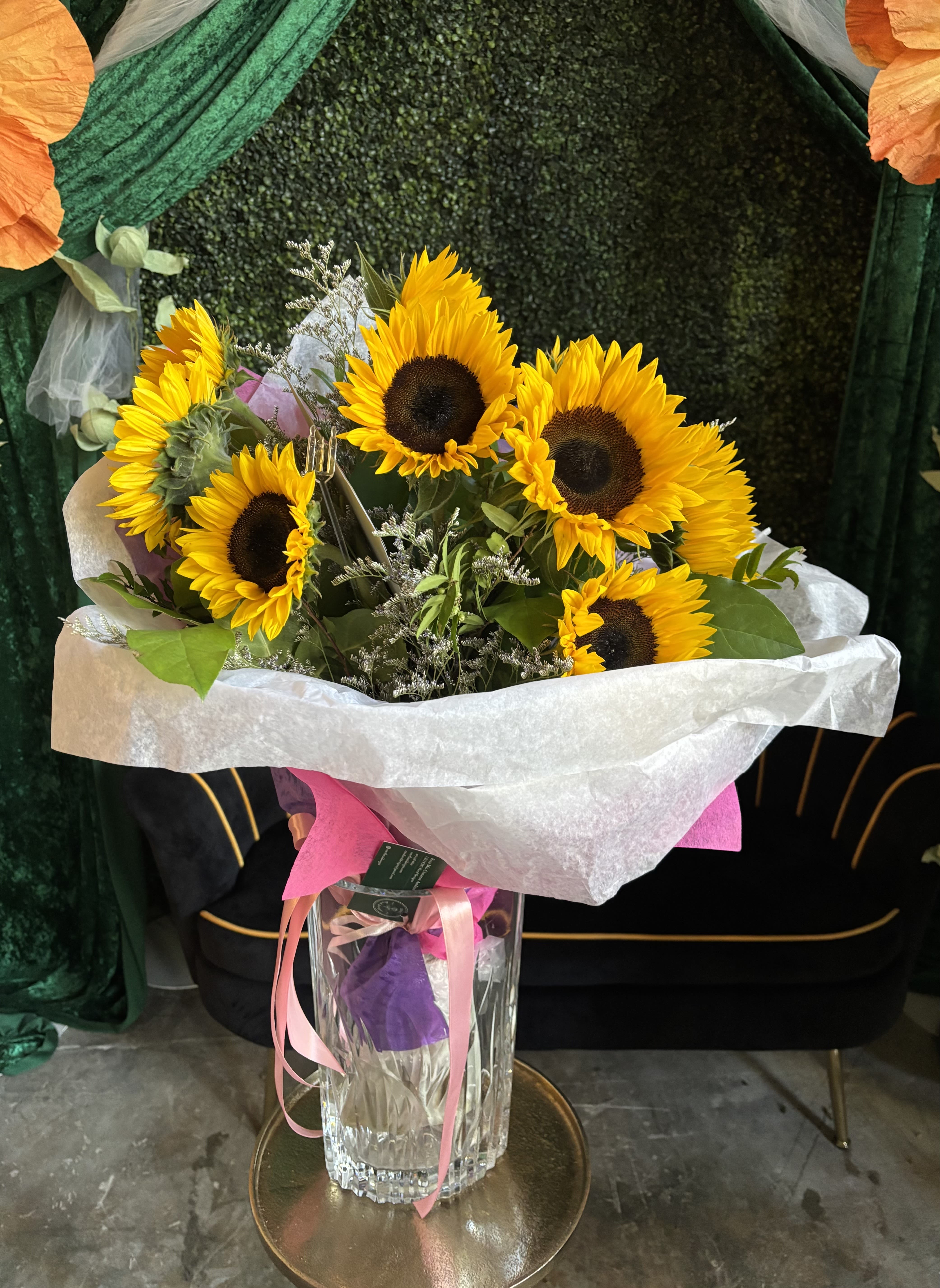 Bouquet of sunflowers in a clear glass vase with pink ribbon