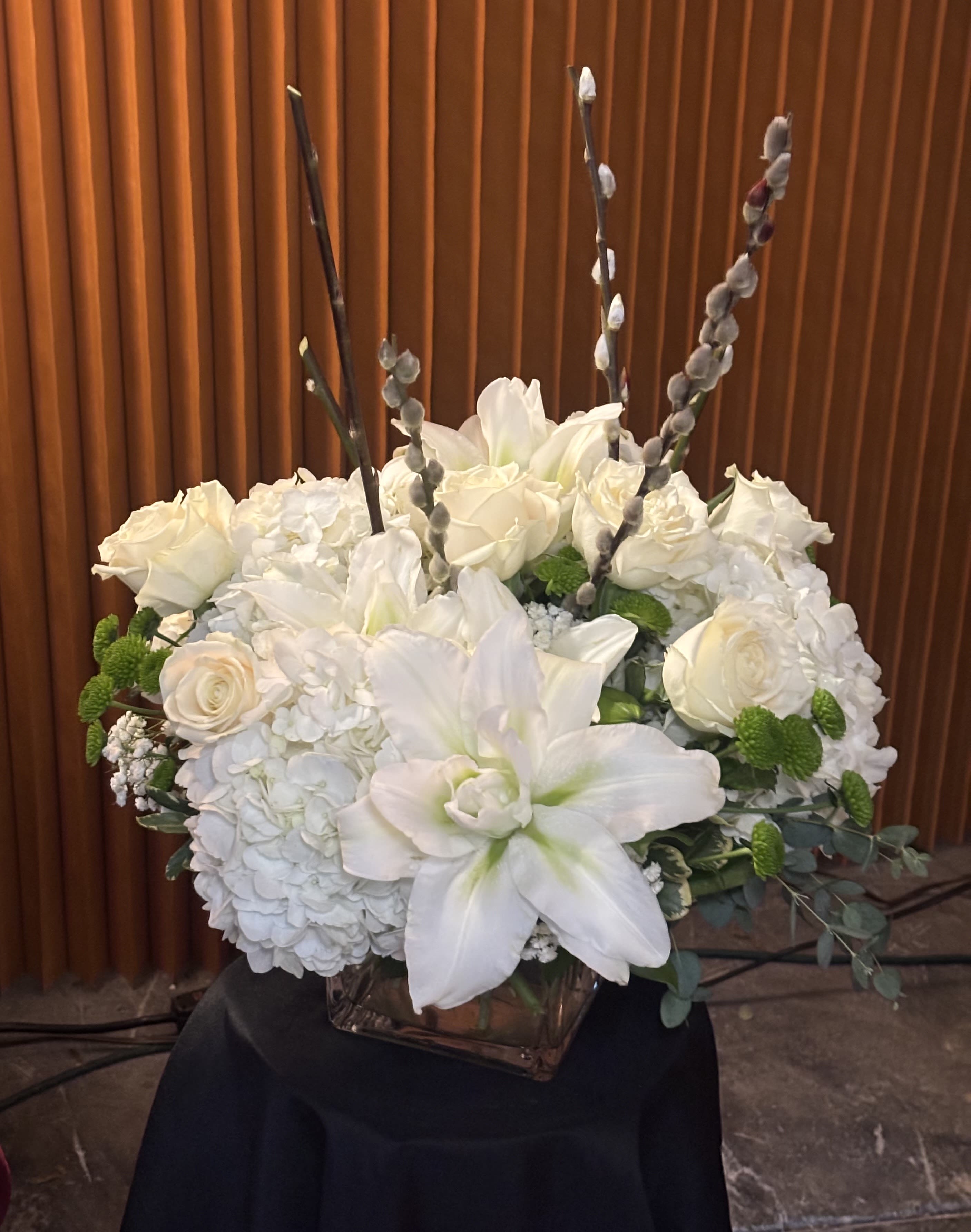 White floral arrangement in a square glass vase with roses and lilies